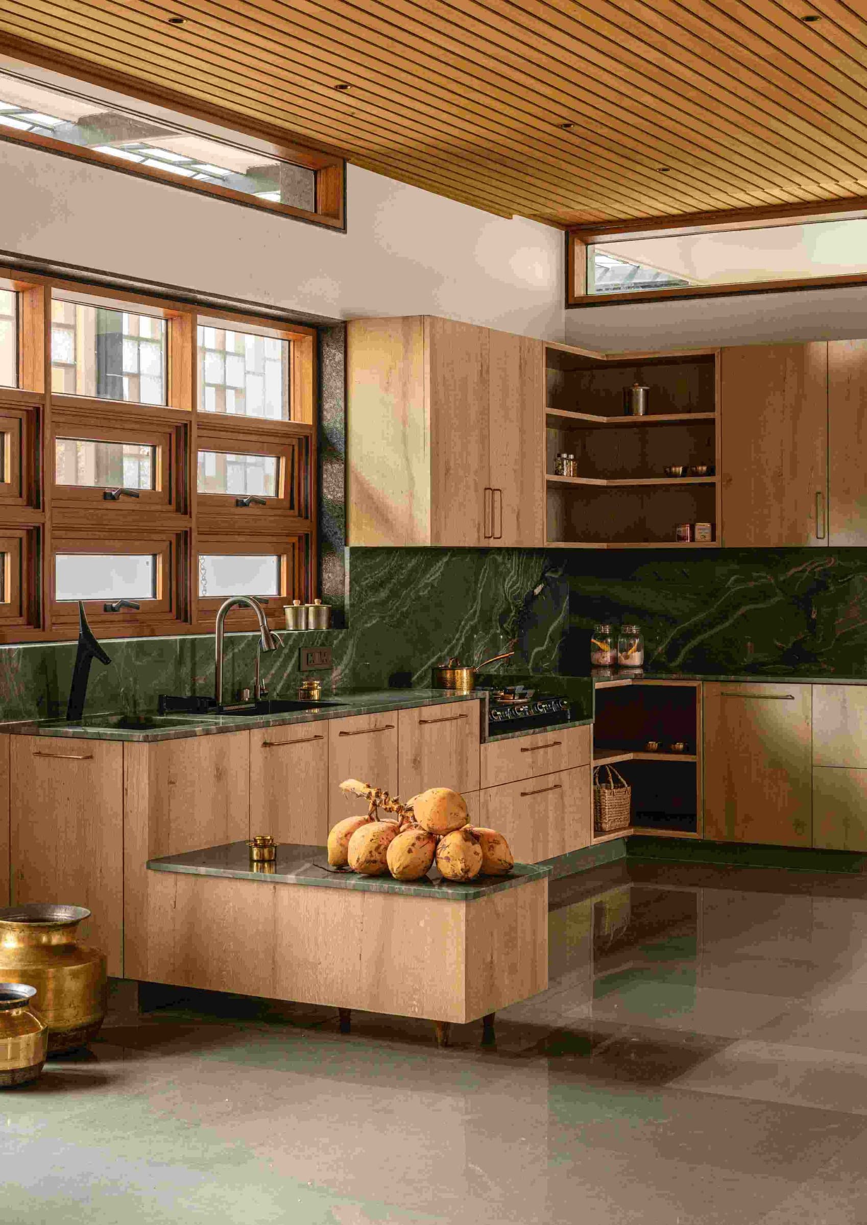 The kitchen, where pale oak cabinetry meets a deeply veined green stone counter under a clerestory of casement windows