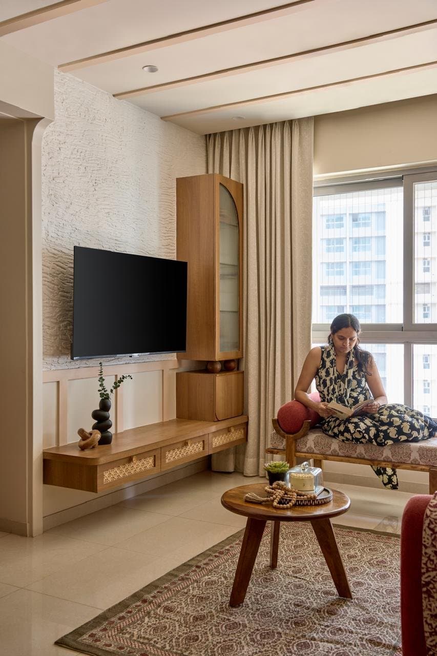 The media wall, where a textured ivory plaster surface meets a cane-fronted wooden console and an arched glass cabinet