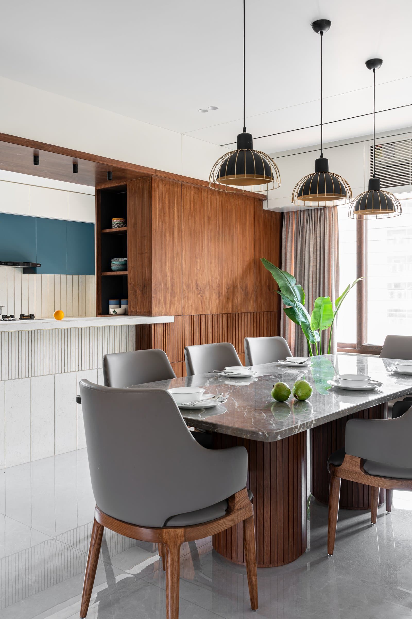 The on-site crafted dining table, its veined stone top echoing the floor, sits beneath cage pendants in matte black and brass