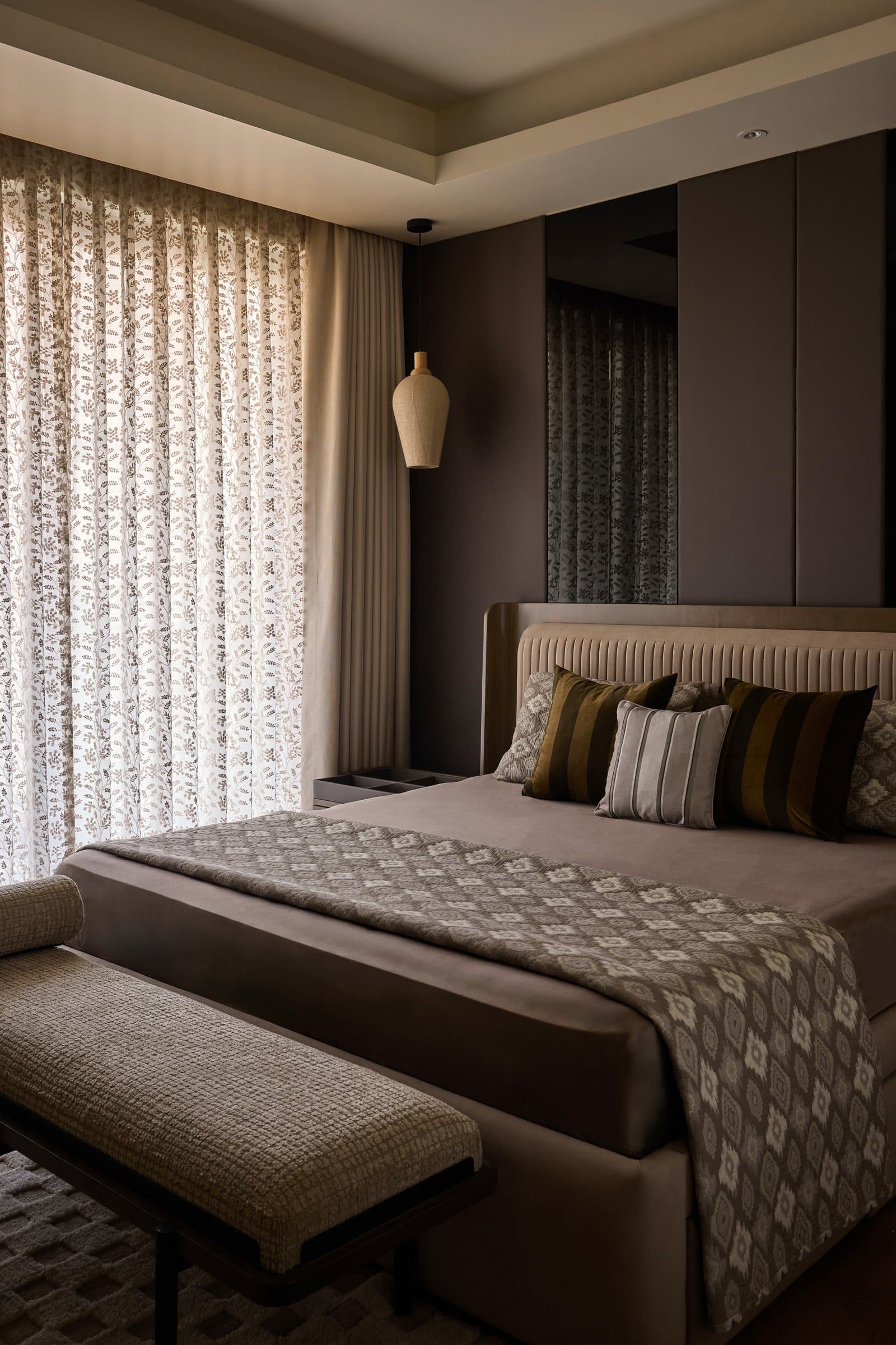 The first bedroom: a channel-tufted taupe headboard, dark panelled walls, and a jute pendant suspended beside the bed