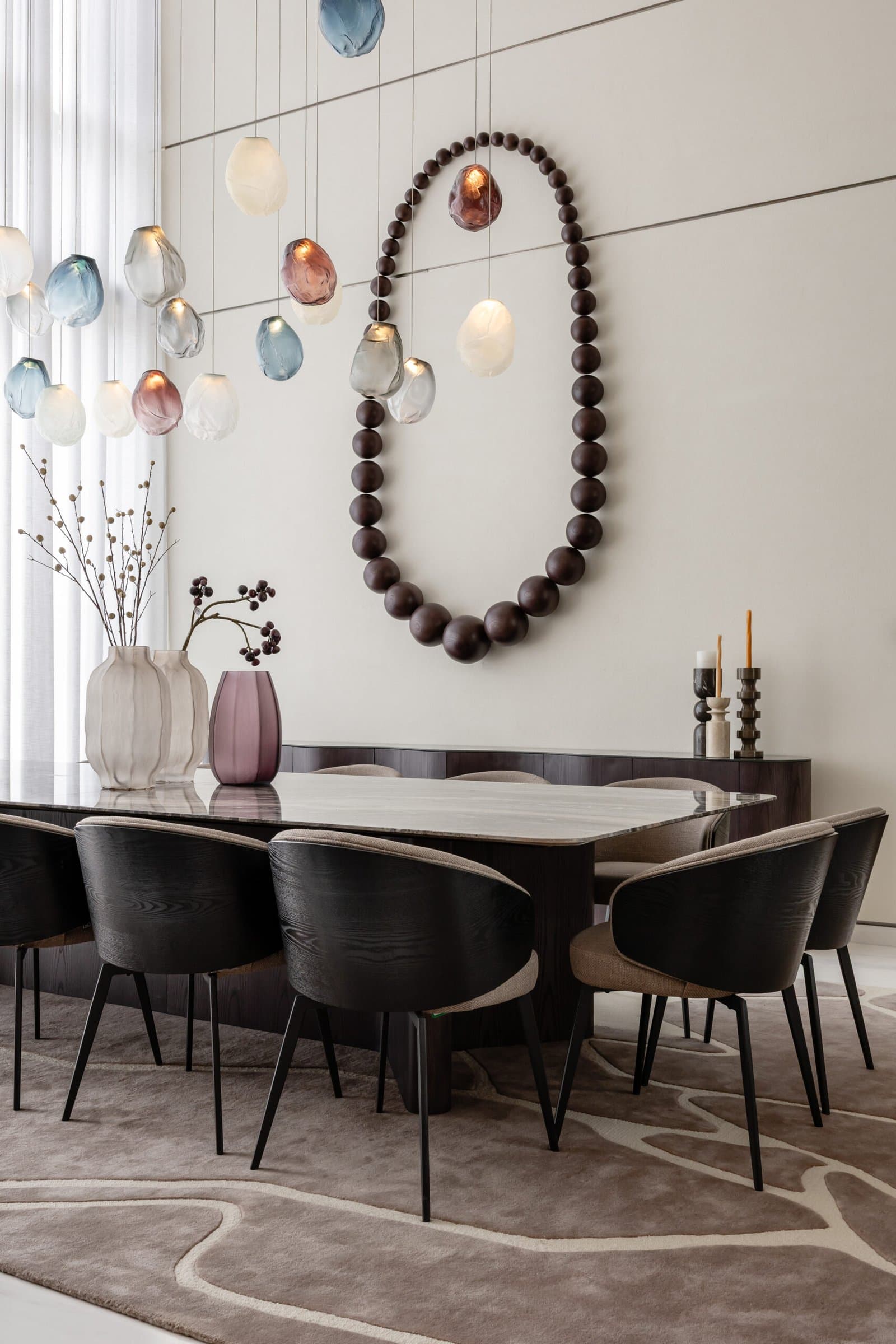 A closer view of the dining wall, where an oval wooden-bead sculpture answers the glass pendants in matte craft