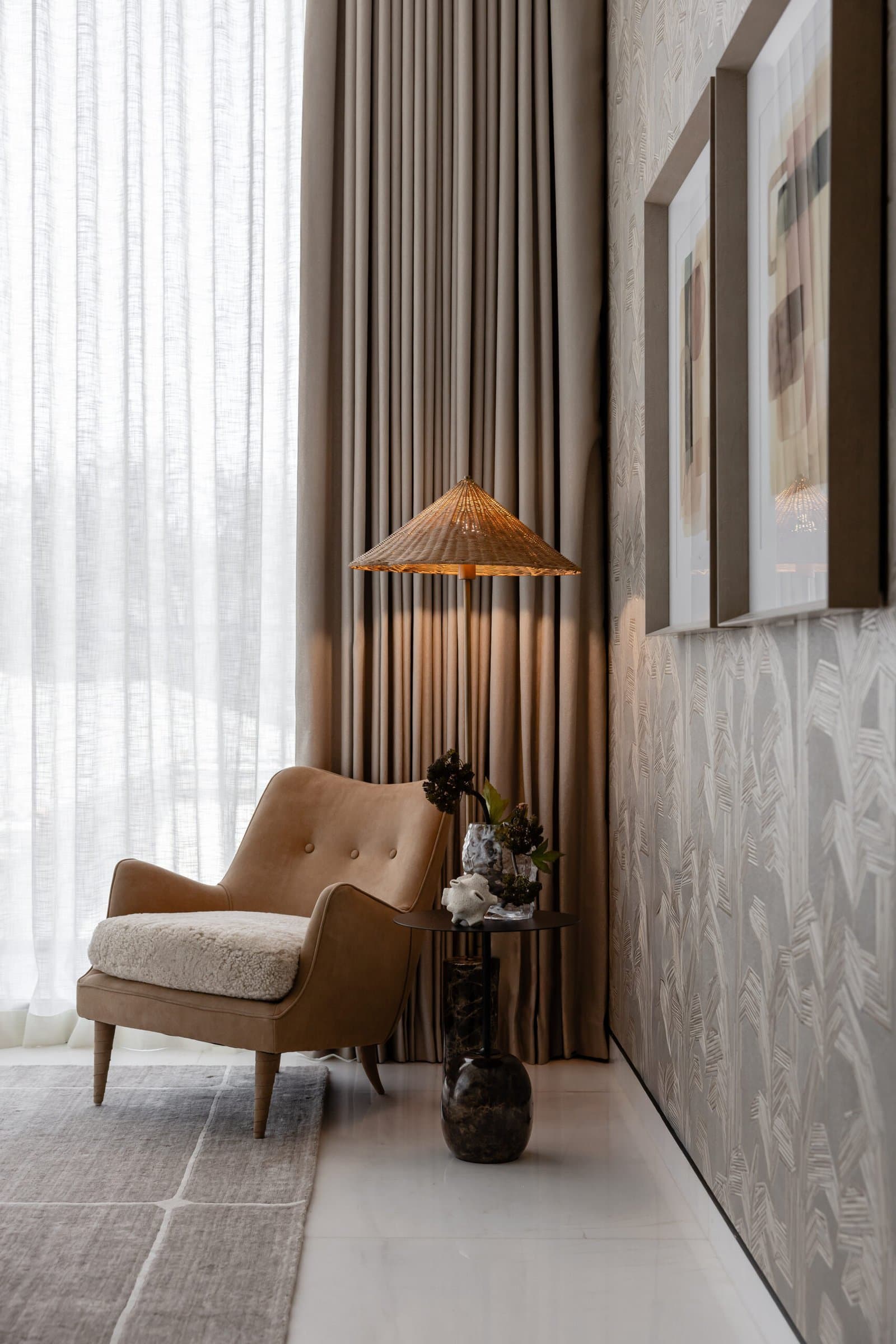 A quiet corner of the bedroom, where a tan suede armchair and a cane-shaded floor lamp settle against patterned wallcovering