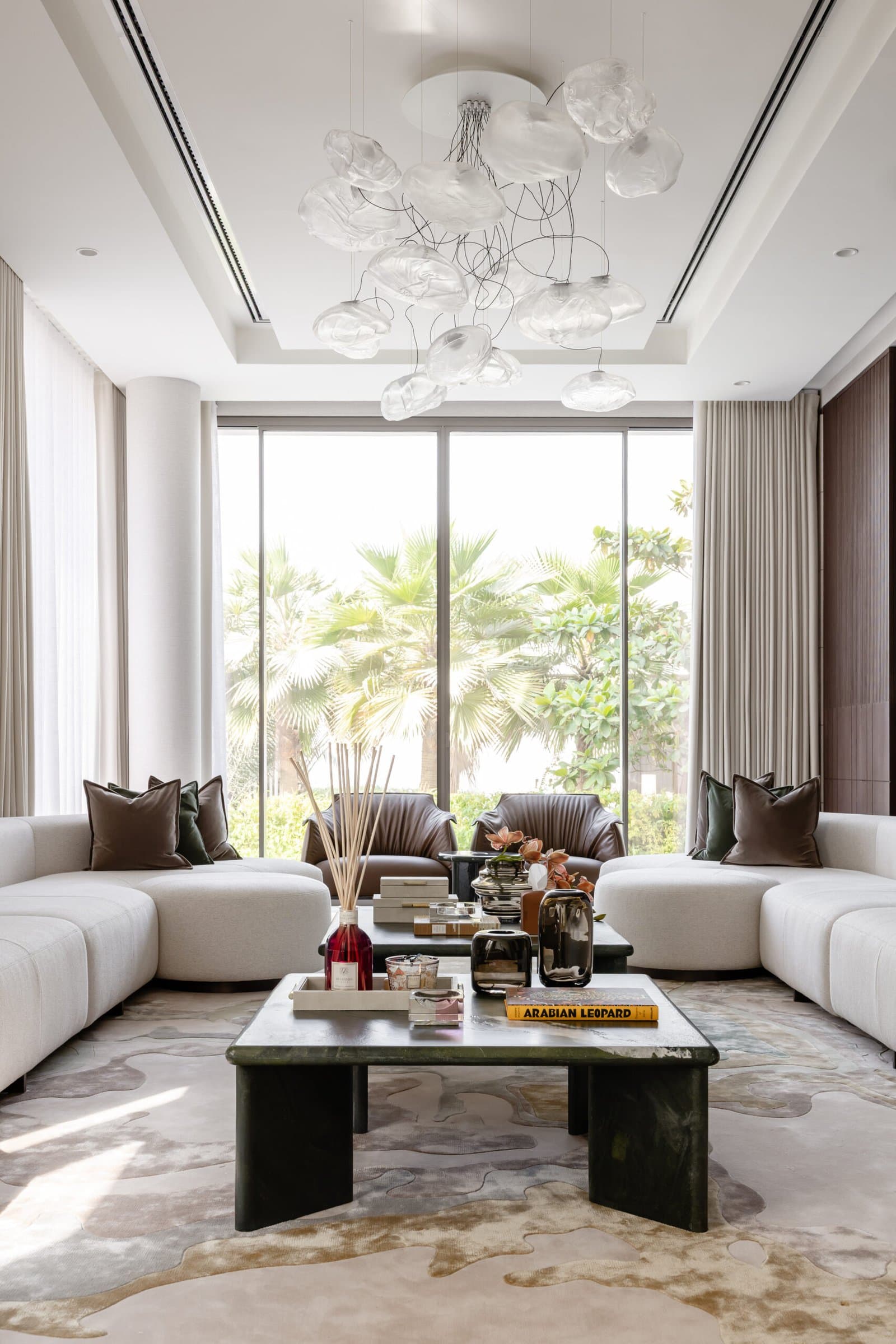 The cloud-like glass chandelier, the room's single permitted extravagance, suspended against floor-to-ceiling garden views