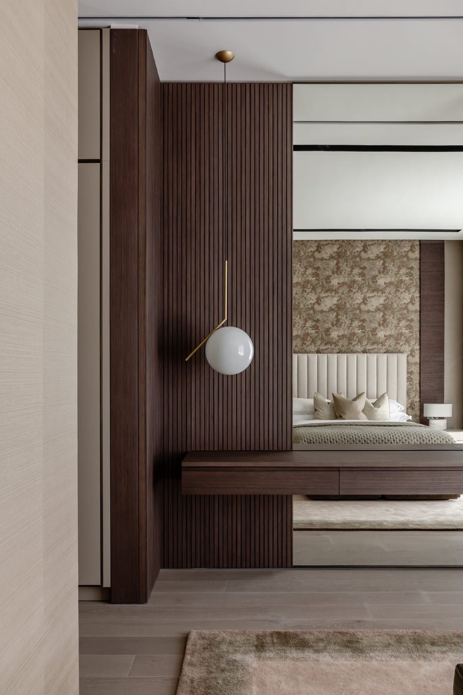 The threshold to the master bedroom: a fluted dark-wood panel, a brass-stem globe pendant, and a glimpse of the channelled headboard beyond
