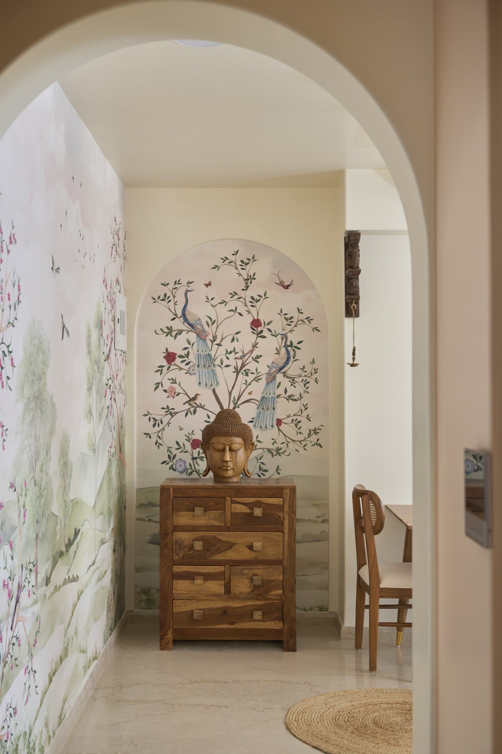 The arrival sequence: a hand-painted peacock mural framed within an arched threshold, anchored by a Buddha on a wooden chest