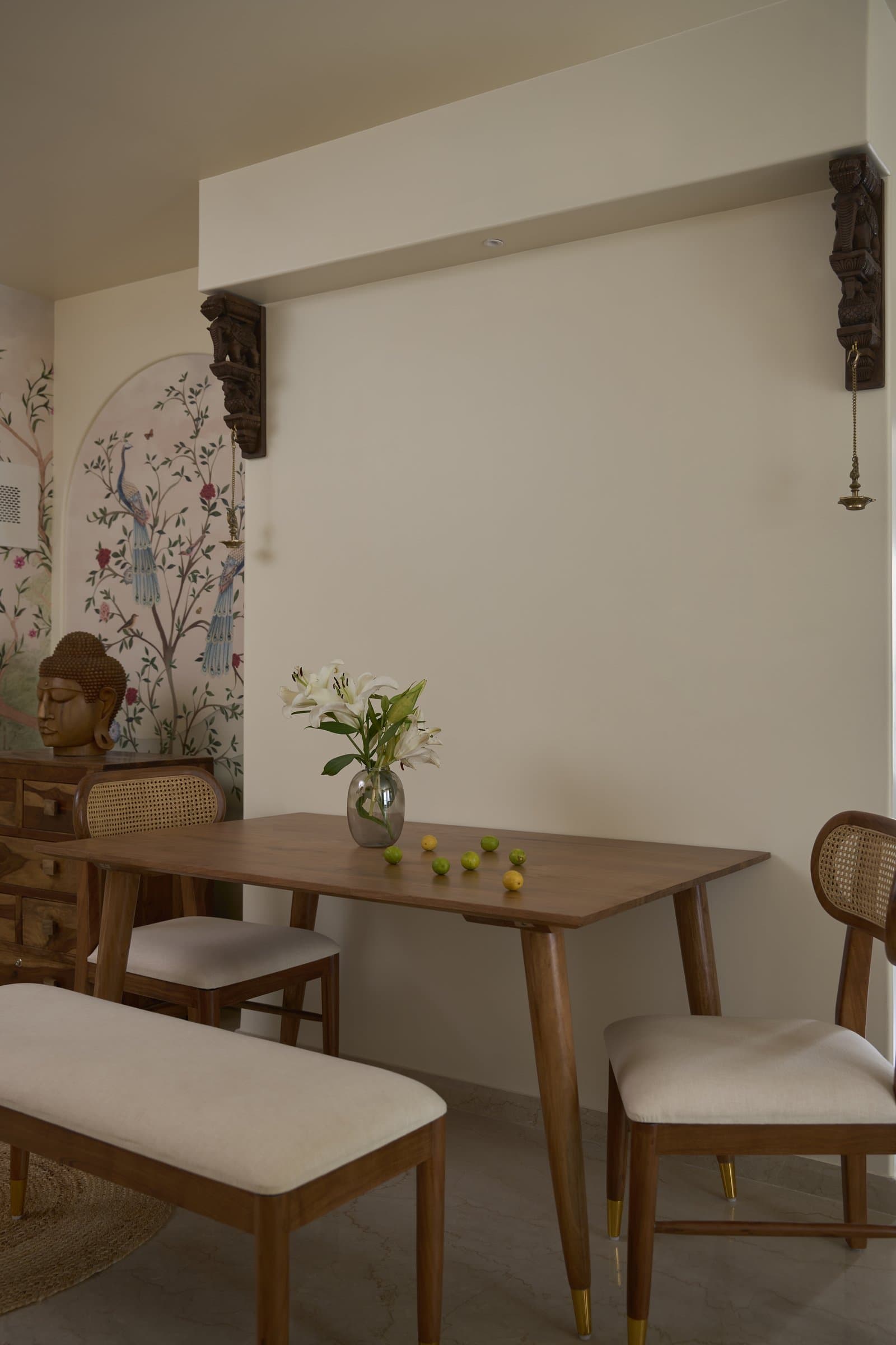 The dining area, sharing its material language with the living room and anchored by a carved corbel and brass diya overhead