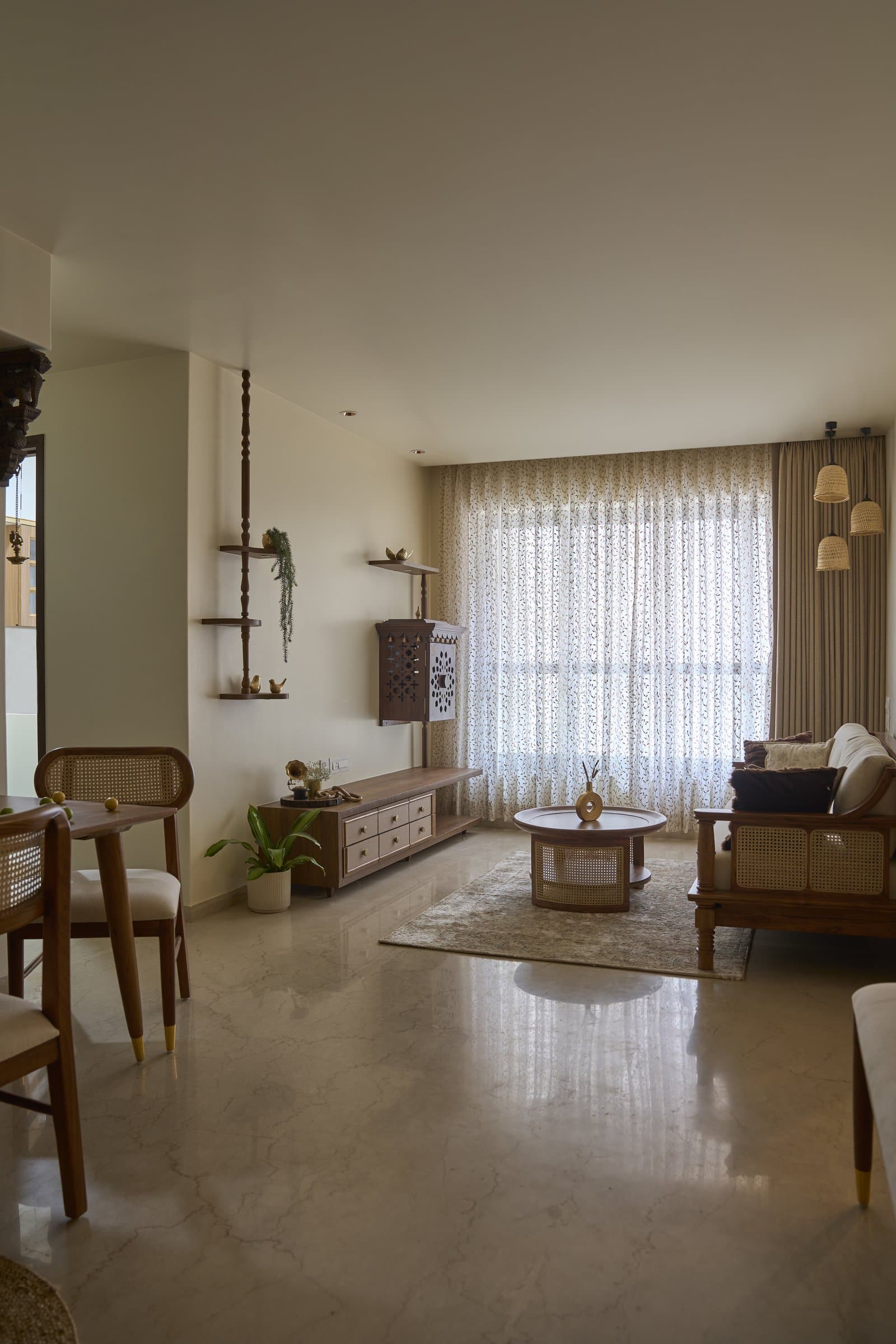 The living room, organised around a single teakwood-and-cane vocabulary, with the floor-to-ceiling proportion doing most of the spatial work