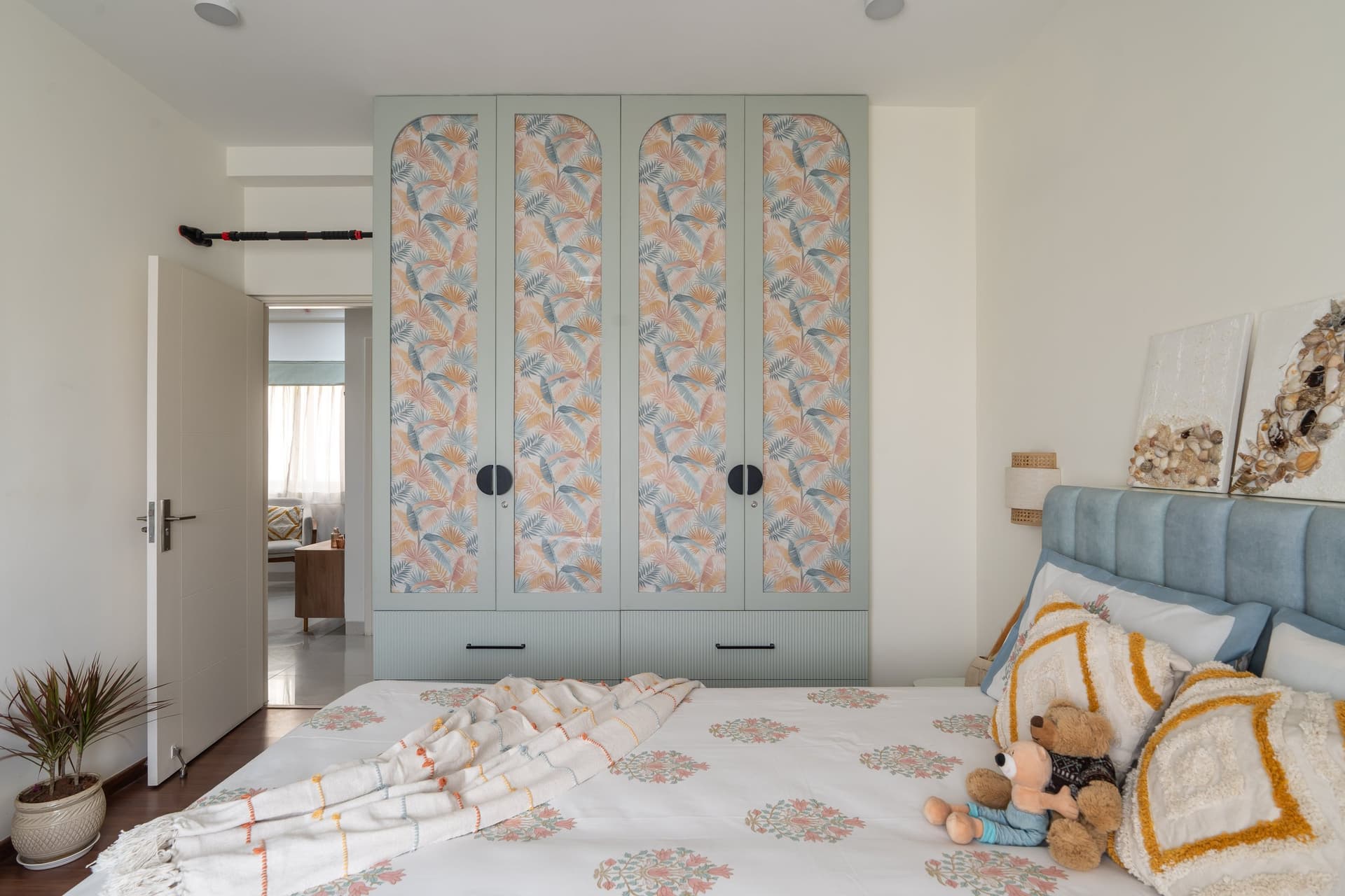 A full wall of sage-green wardrobes with arched panels of tropical-leaf wallpaper