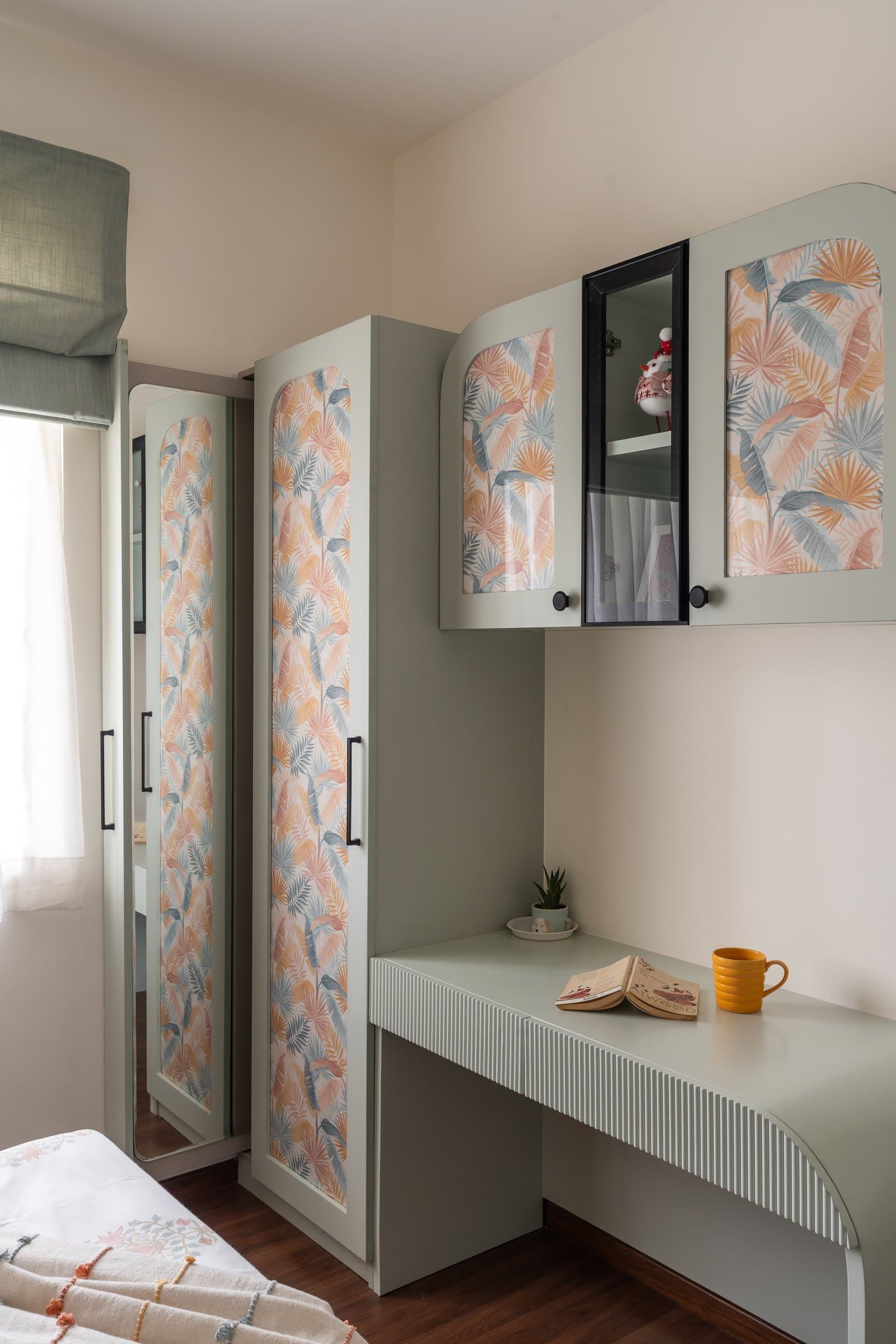 The study nook beside the wardrobe, with a fluted sage desk continuing the room's botanical vocabulary