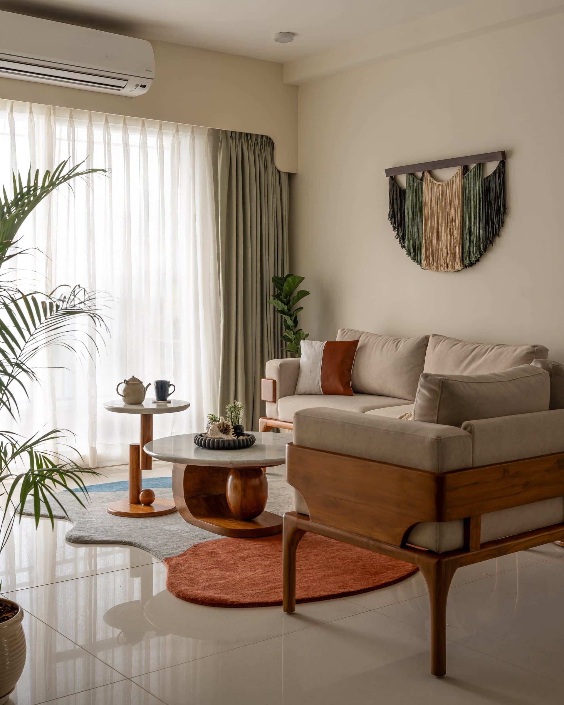 In the living room, a linen sofa and sculptural coffee table sit beneath a macramé hanging in sage and oat tones