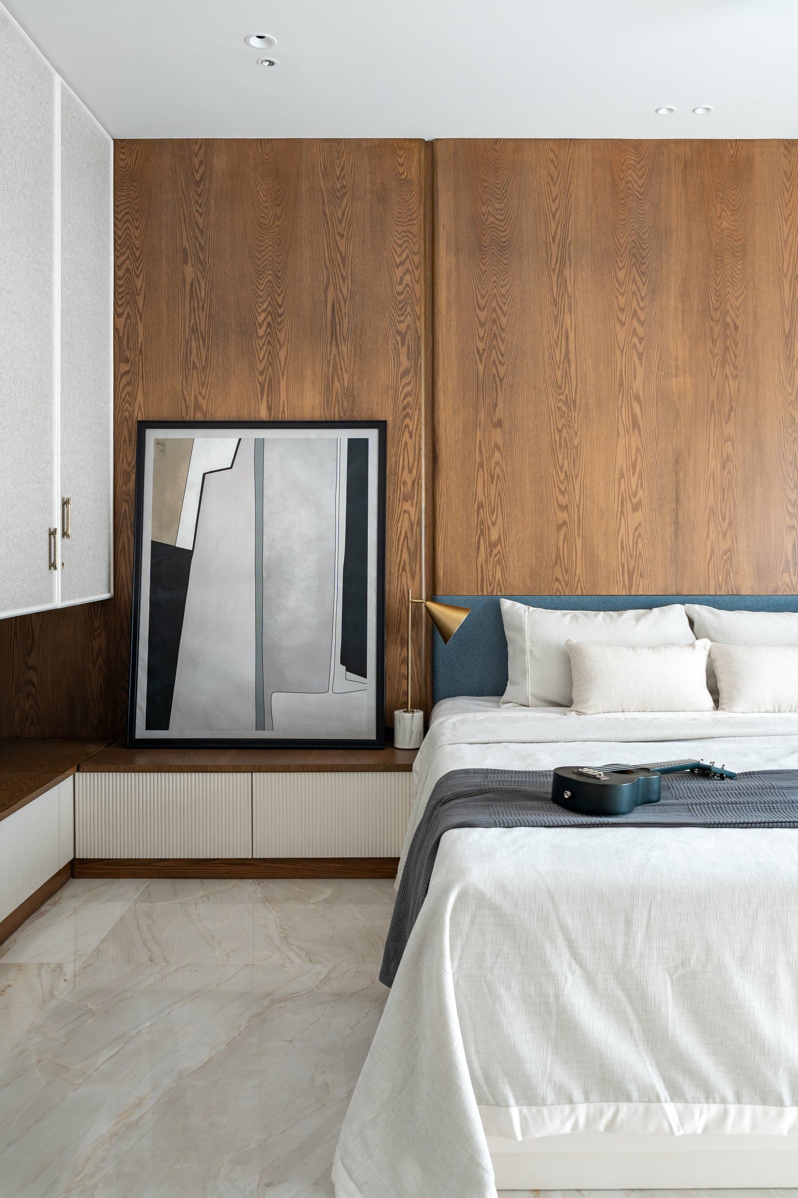 An oak-panelled headboard wall absorbs sound and light, with a leaning canvas in place of a hung one