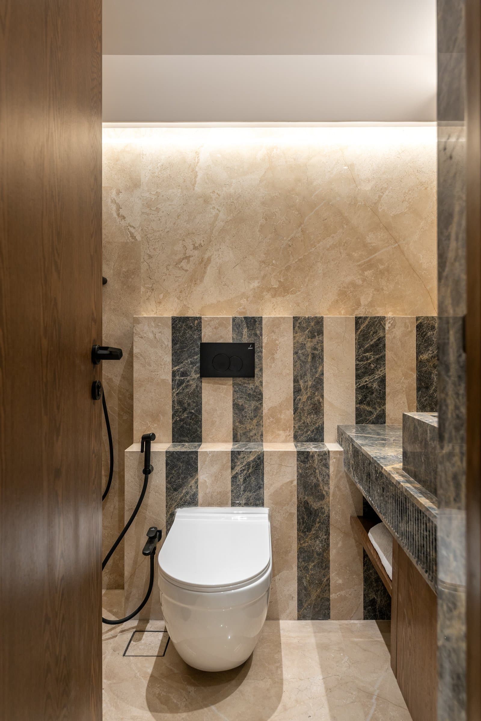 Striped panels of dark green-grey and warm beige stone reinterpret the home's green-stone motif as graphic rhythm