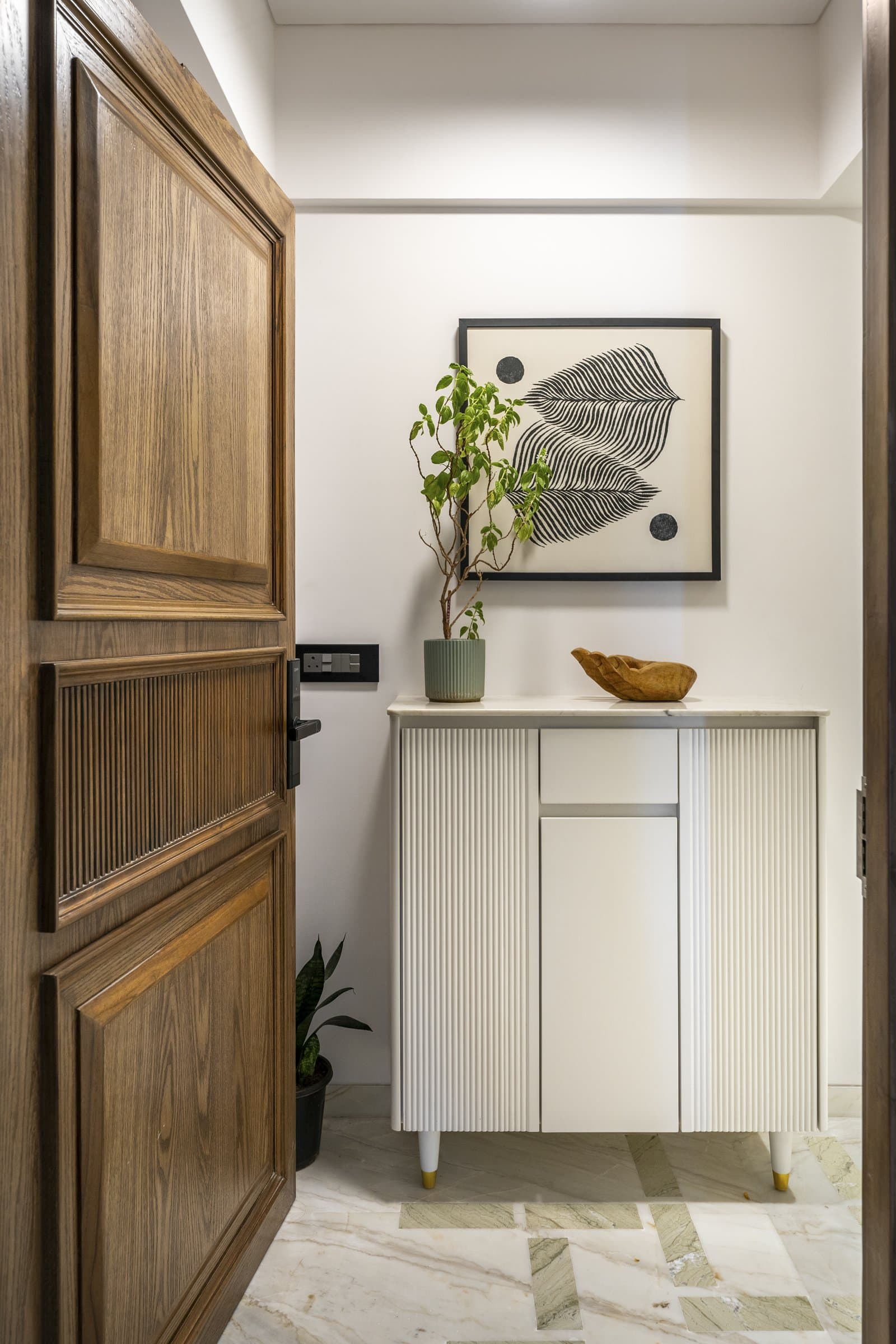 The foyer: a panelled oak door, a fluted ivory console, and a marble inlay floor that introduces the home's green-veined stone before the living room reveals it