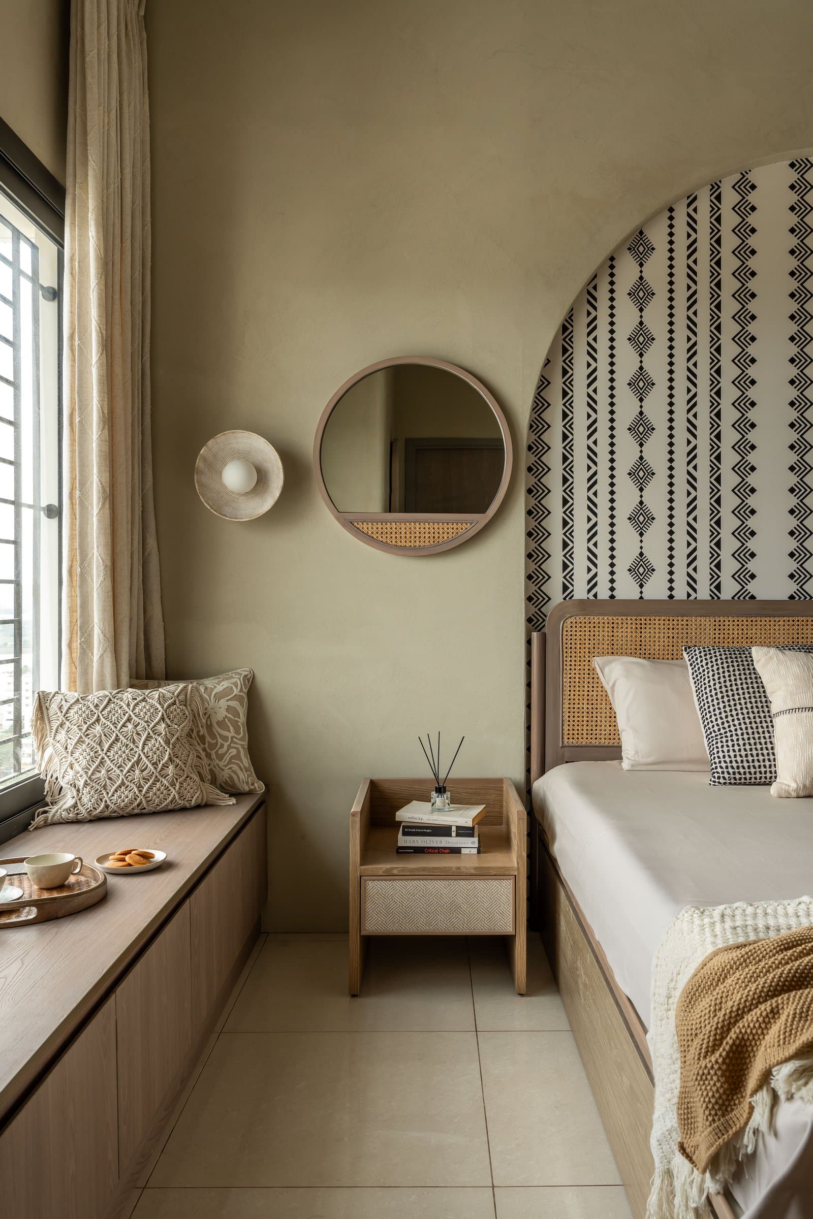 The window seat and circular caned mirror extend the bedroom's quieter life
