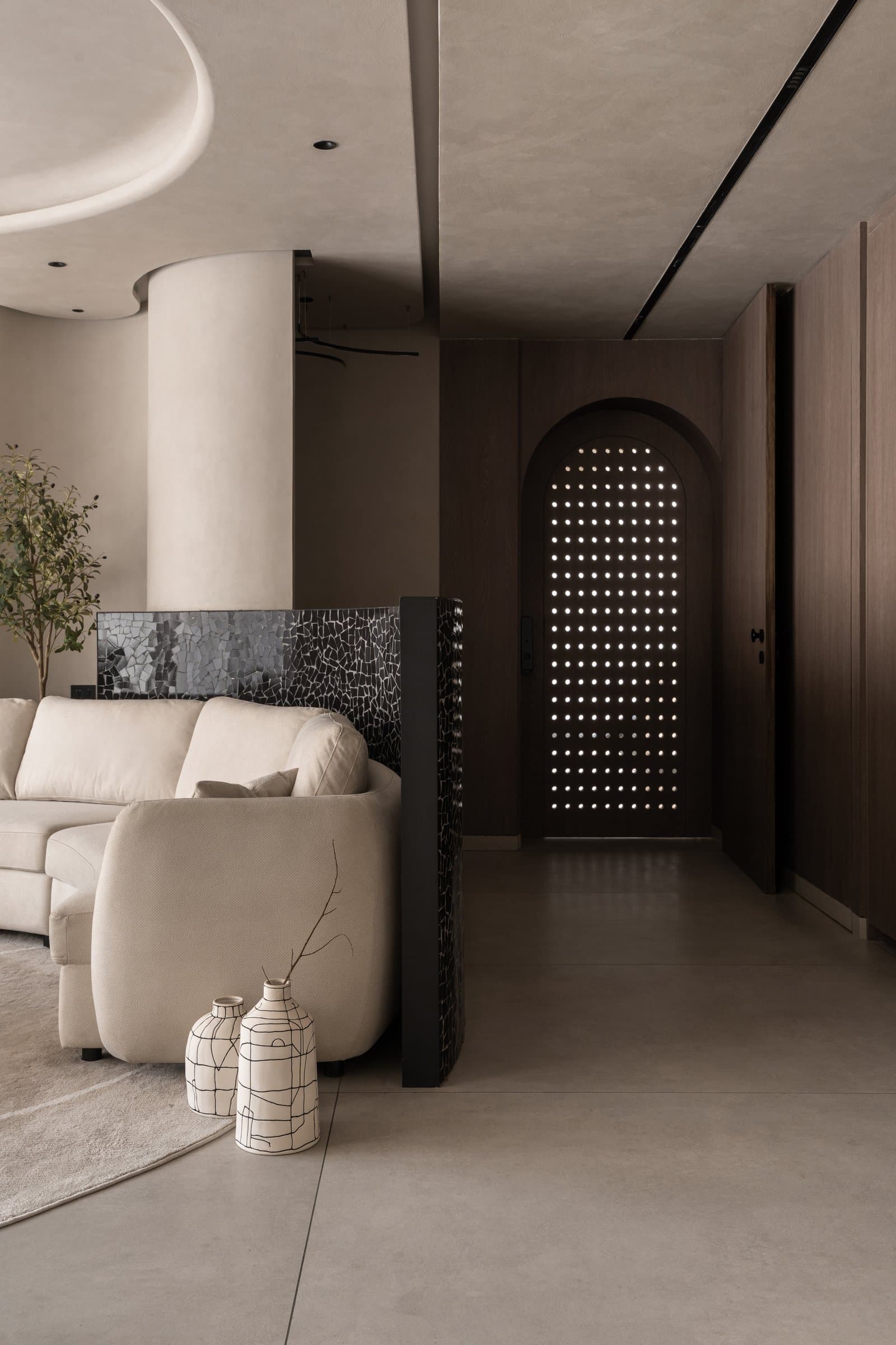 Seen from inside, the perforated door reads as a luminous screen, with the curved soffit and mosaic divider introducing the project's material vocabulary