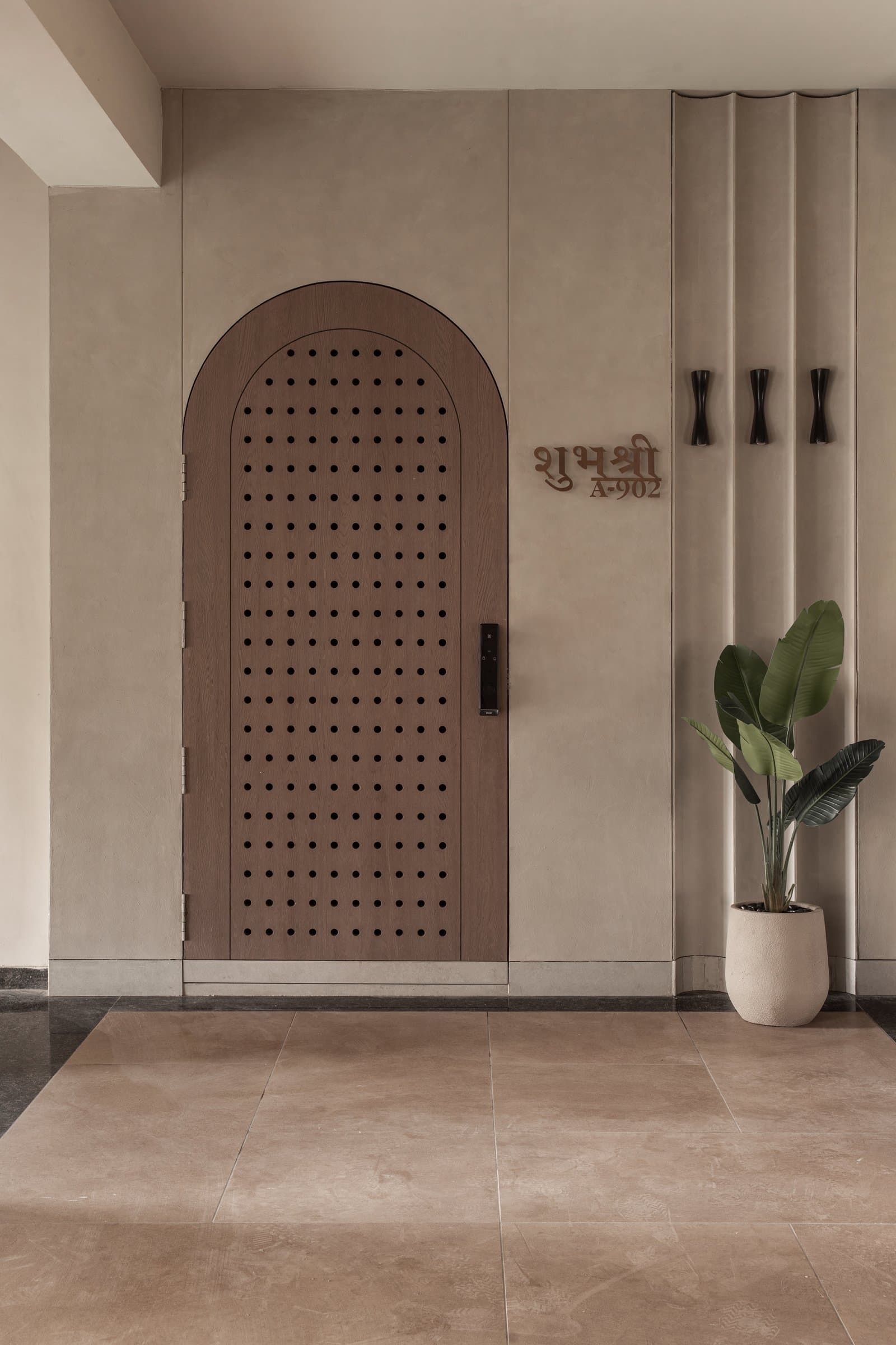 The entry: an arched, perforated wooden door set against fluted plaster establishes the home's central geometry before the apartment begins