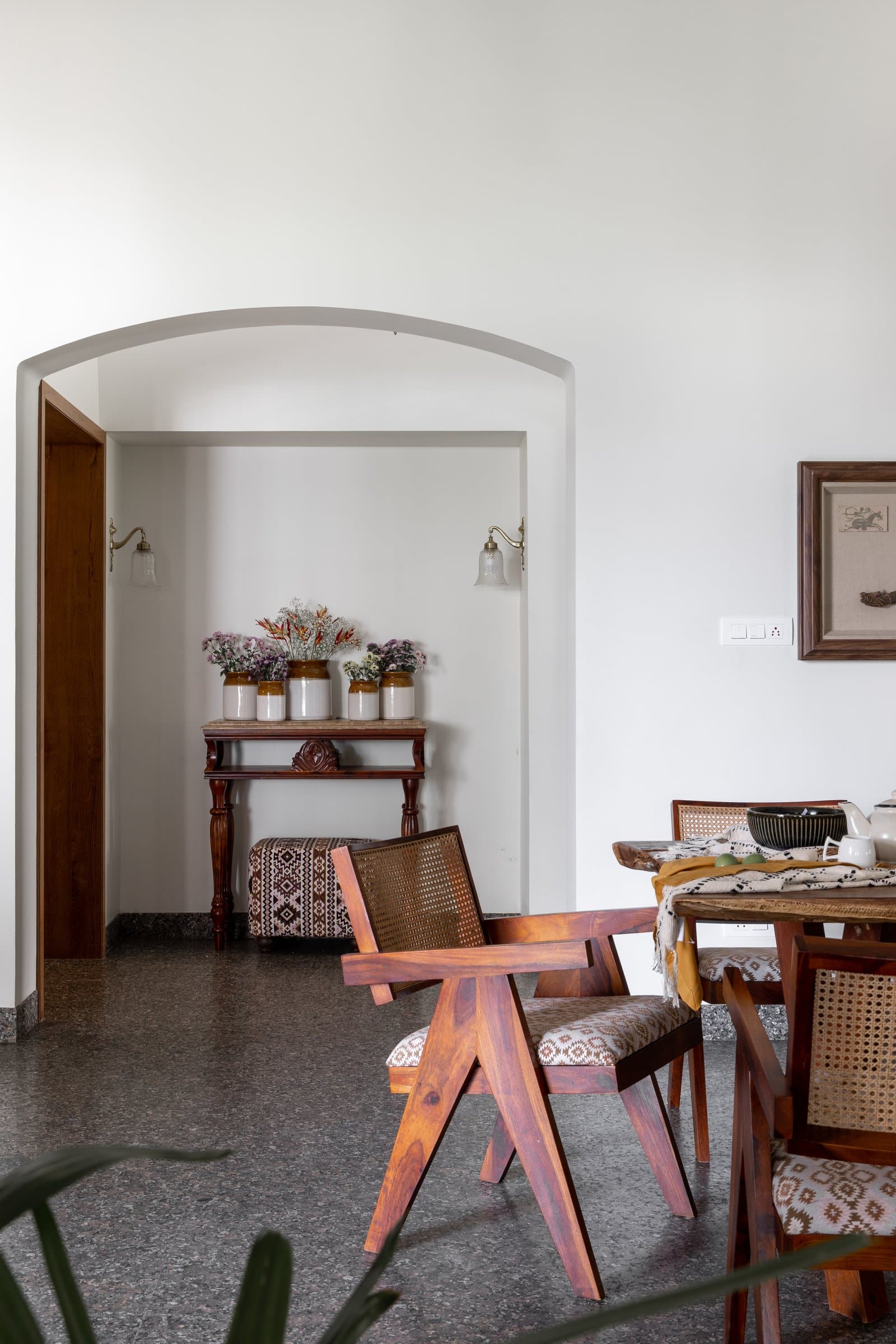 A soft plastered arch frames the entry vignette, anchored by a Chandigarh-language armchair in honey-toned sheesham