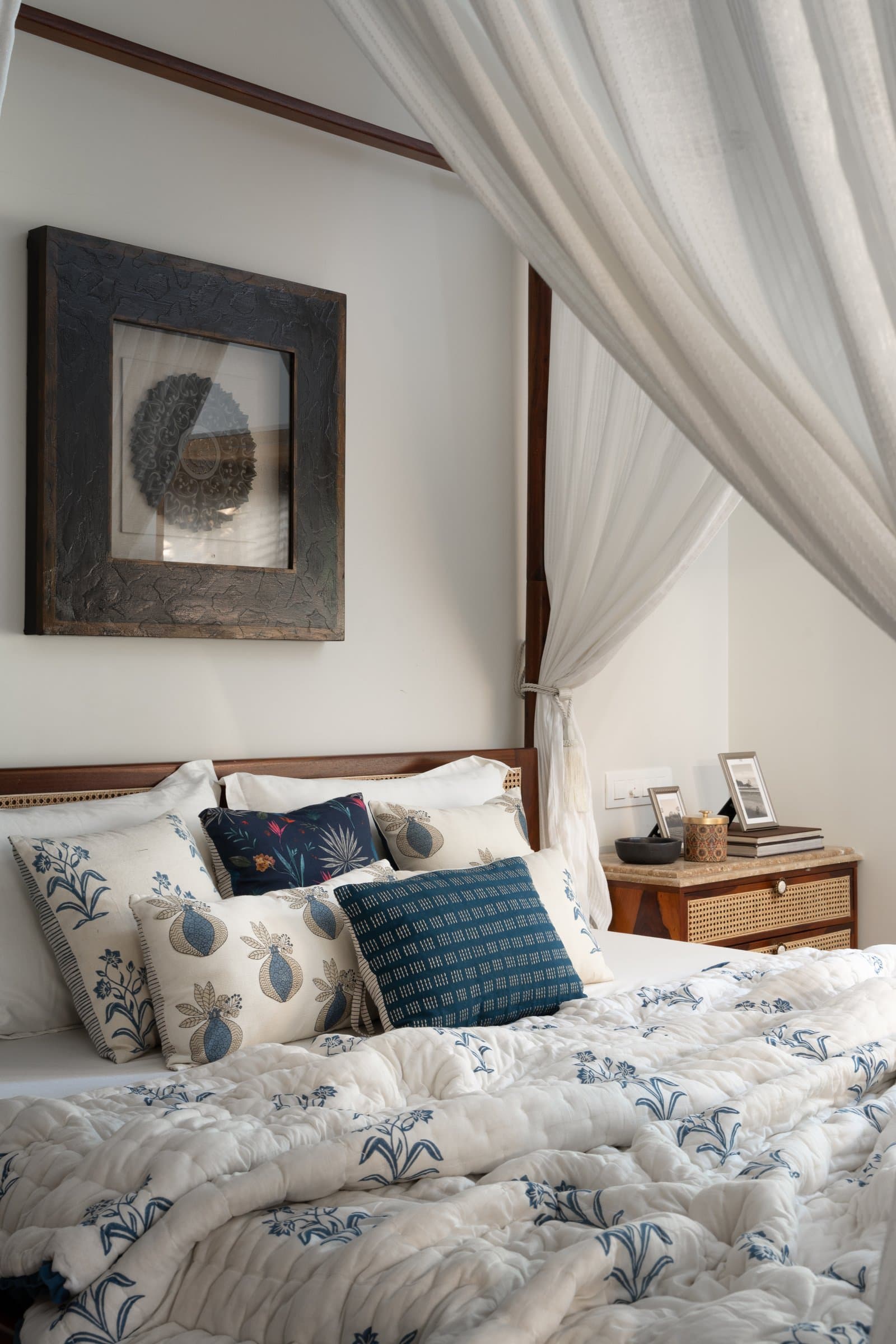 A heavily-textured charcoal artwork and a caned bedside chest layer the headboard wall in quiet detail