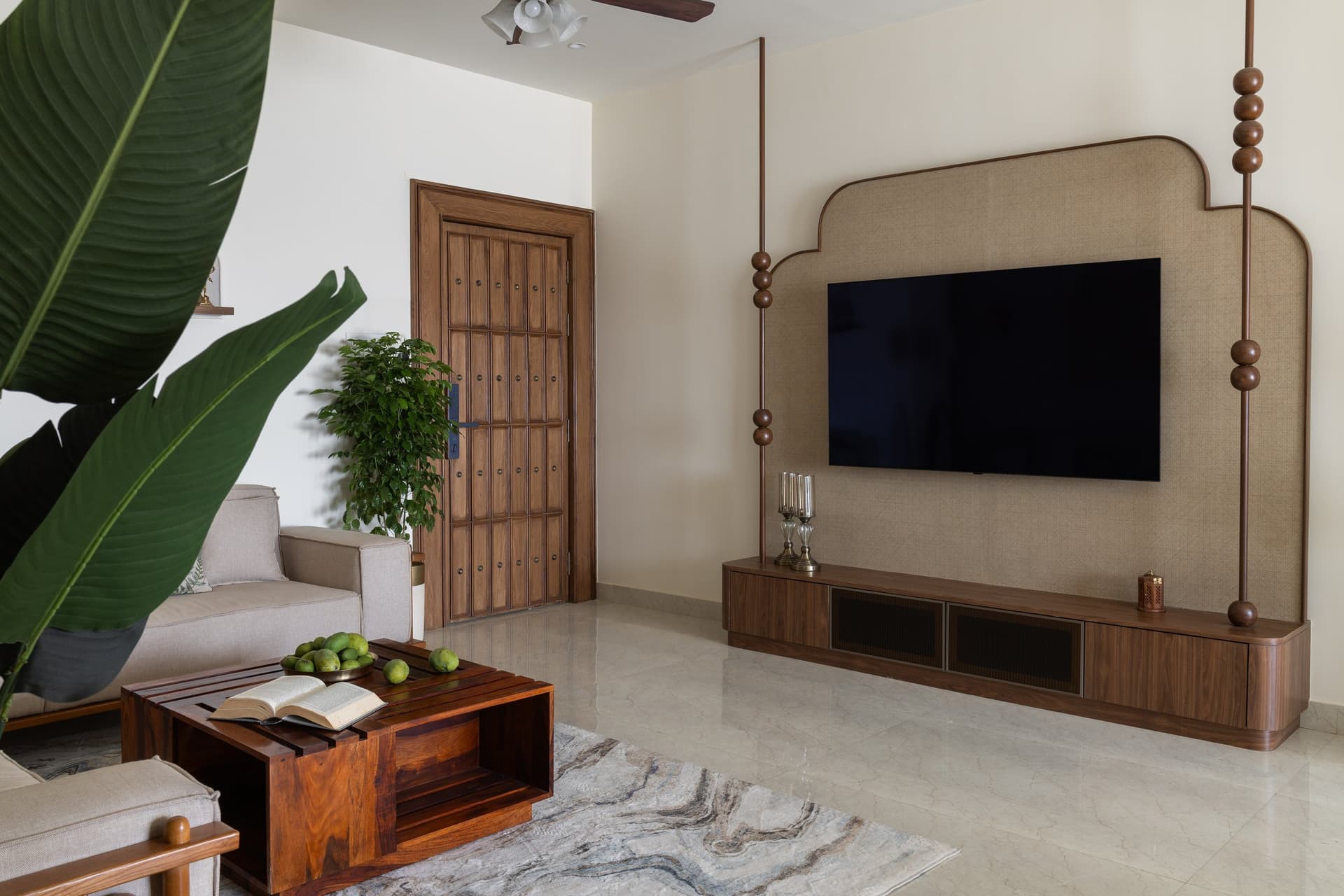 The television wall, where a linen-clad stepped panel and slender bead-threaded posts hold the room's one sculptural gesture