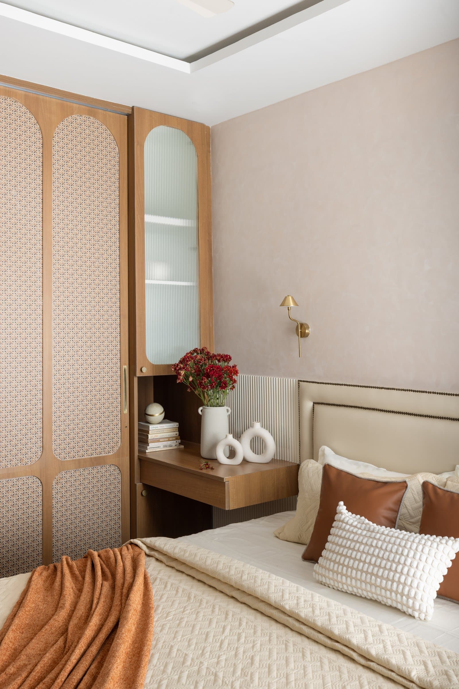 The primary bedroom, where a studded headboard and cane-inlay wardrobe shutters keep the room reading as repose rather than utility