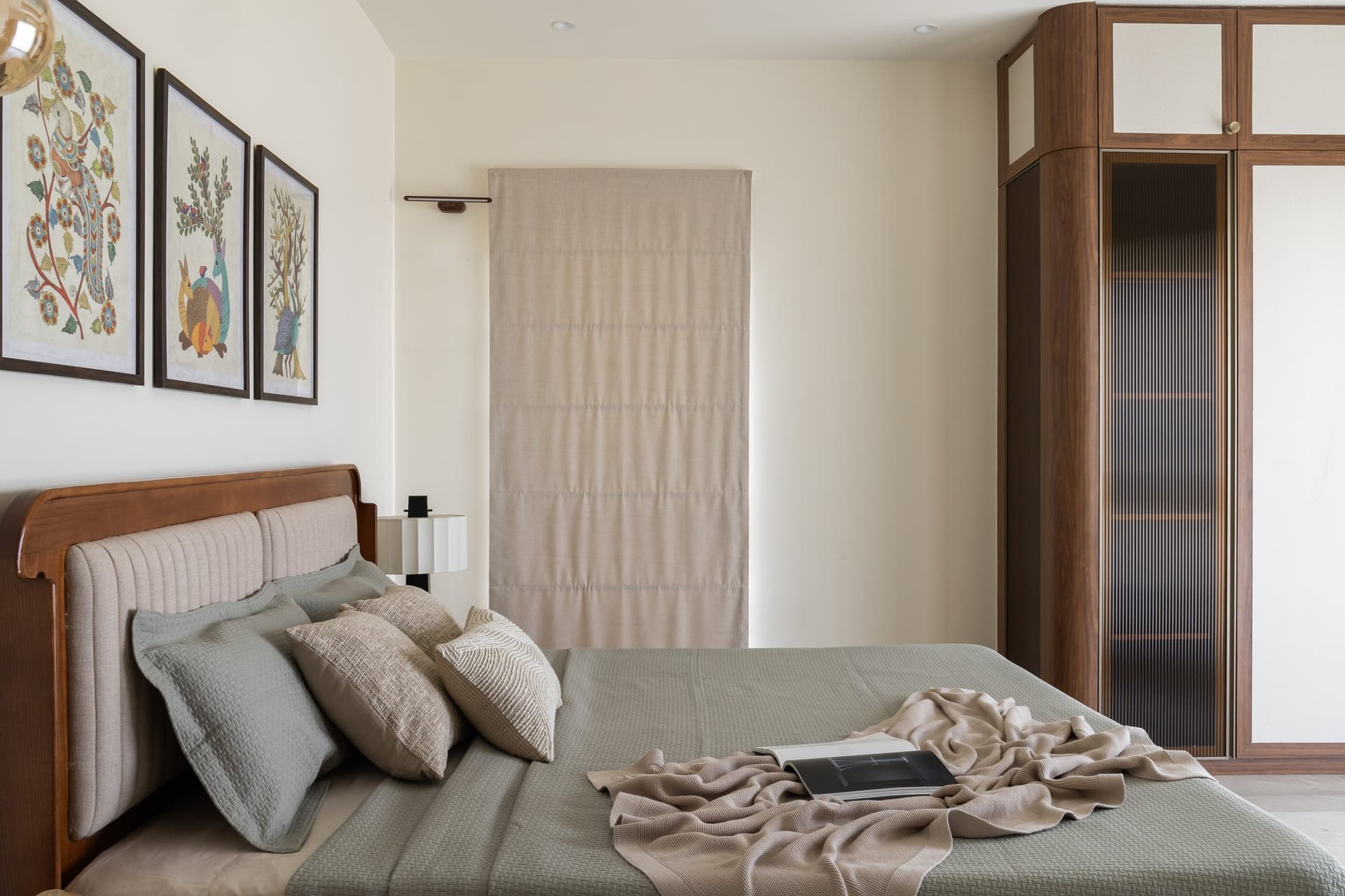 The bed wall, anchored by a curved upholstered headboard and a triptych of folk-art prints in ochre, teal, and rust