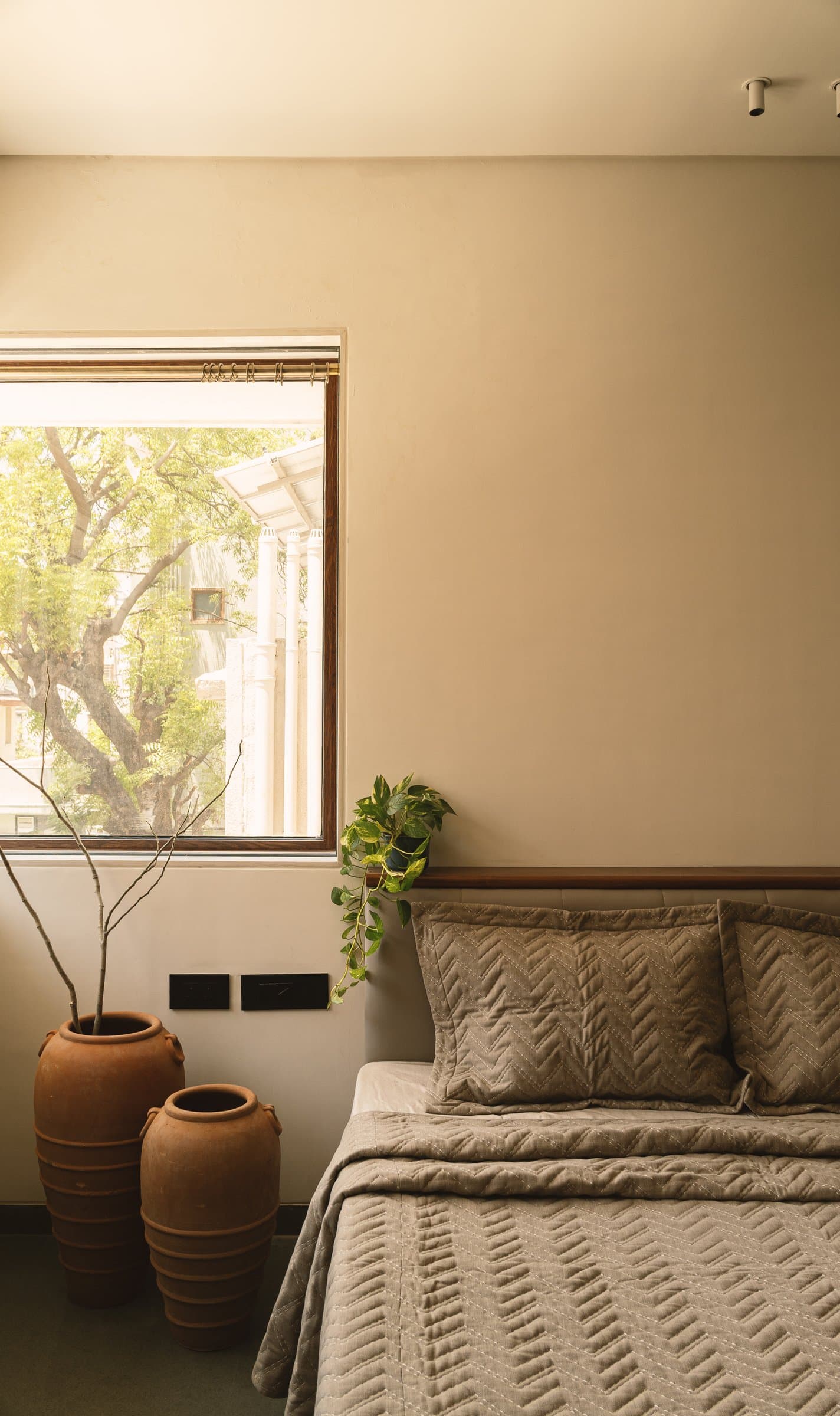 A closer view: low upholstered headboard, soft sand walls, and a pair of terracotta vessels working as slow furniture