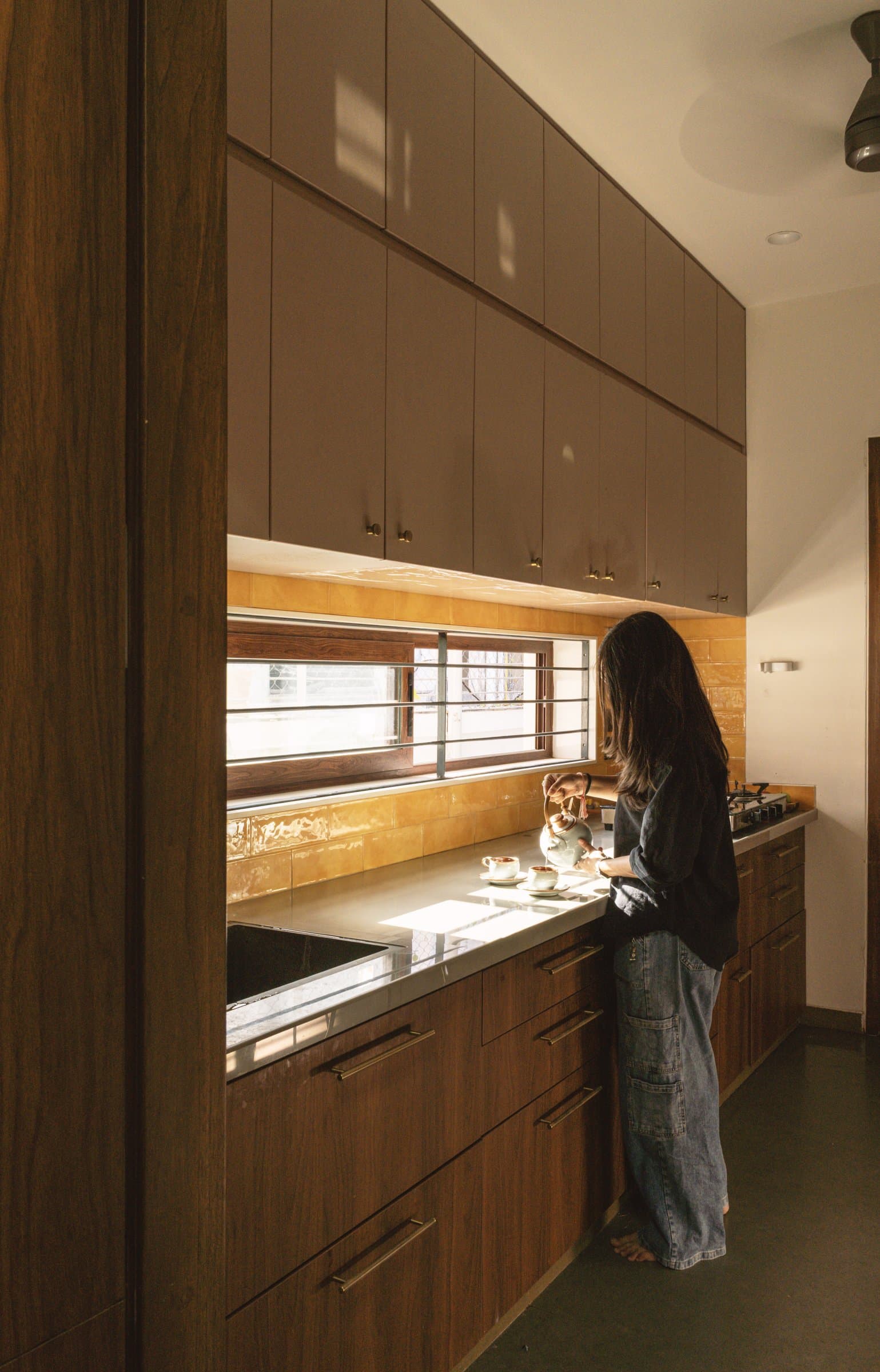 In the galley kitchen, mauve-grey upper cabinetry meets warm wood below, separated by a band of honey-toned glazed tile