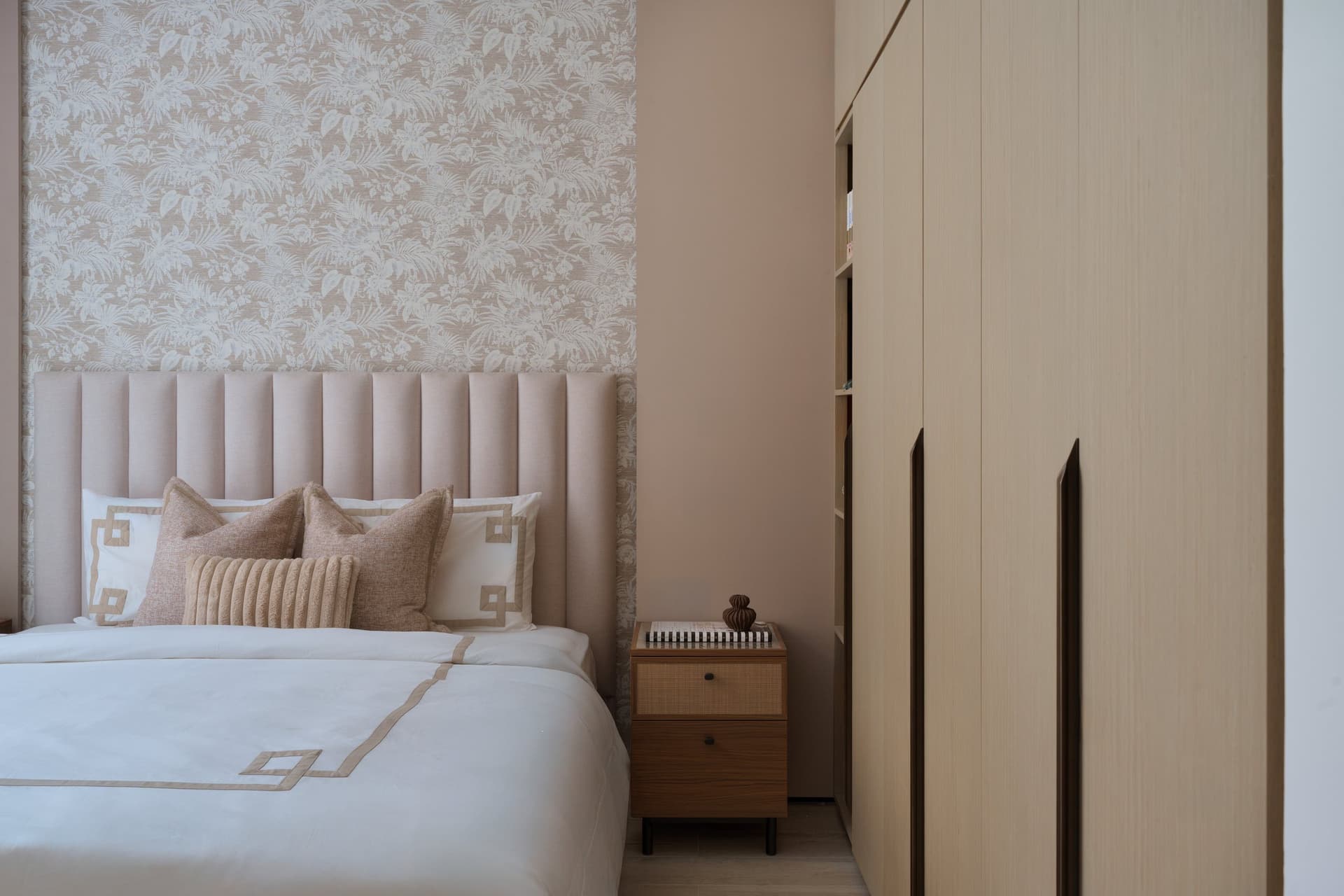 The second bedroom, where built-in oak wardrobes dissolve into the wall plane and leave the blush headboard to do the visual work