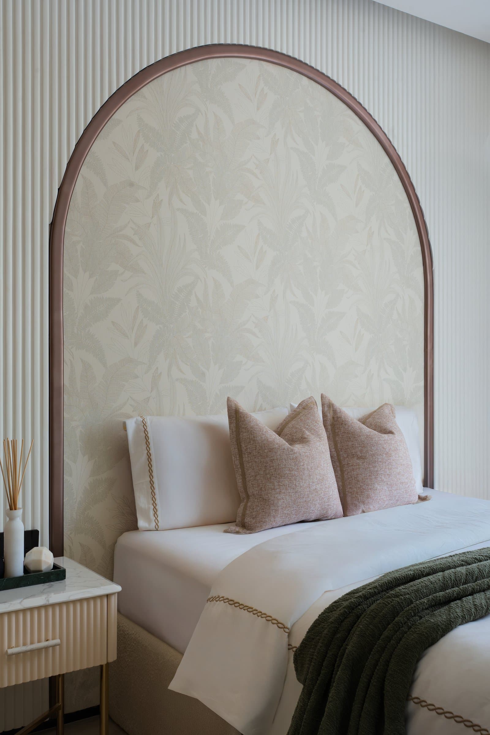 The guest bedroom, where an arched headboard wall in copper-framed botanical print sits within fluted ivory panels