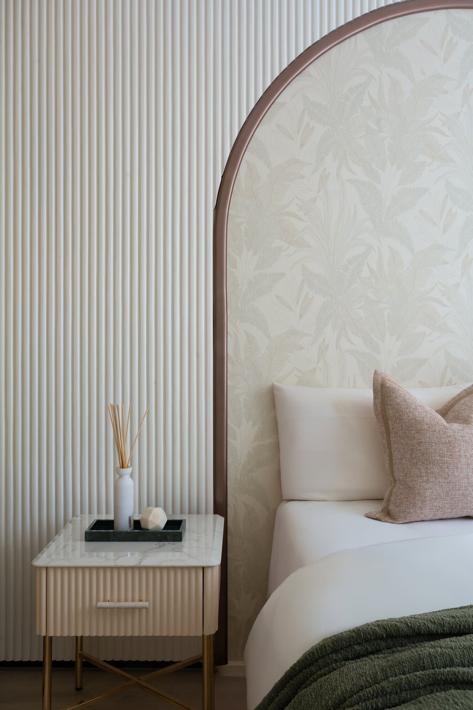 The arched headboard resolving against the fluted wall, with a slim stone-topped bedside cabinet completing the composition
