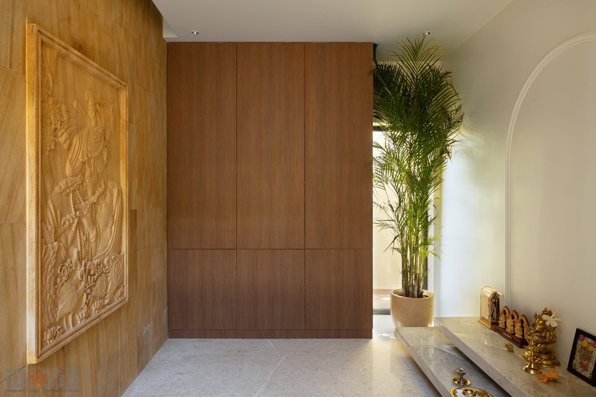 A carved sandstone relief and fluted teak joinery hold the puja niche; tradition folded into the architecture rather than displayed