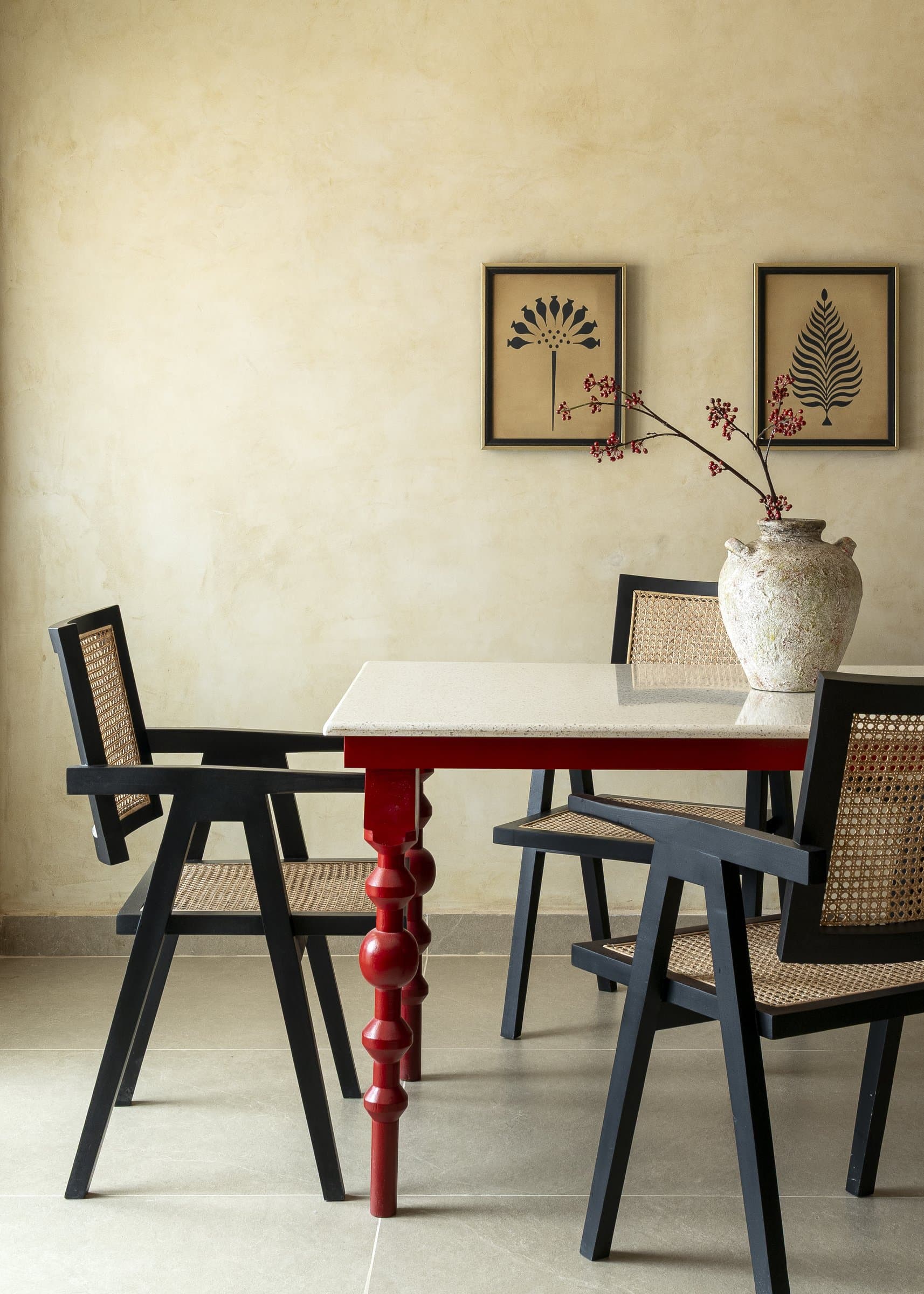 The dining table's scarlet duco-painted legs and turned silhouette, the home's most theatrical decision, set against a weathered terracotta urn