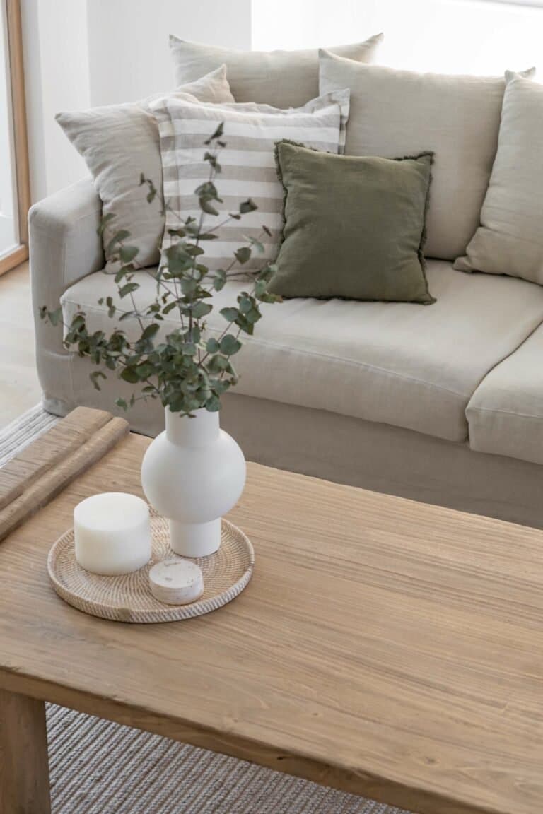 The coffee table vignette: rattan tray, ceramic vase, eucalyptus stems; the project's restraint distilled into a single still life