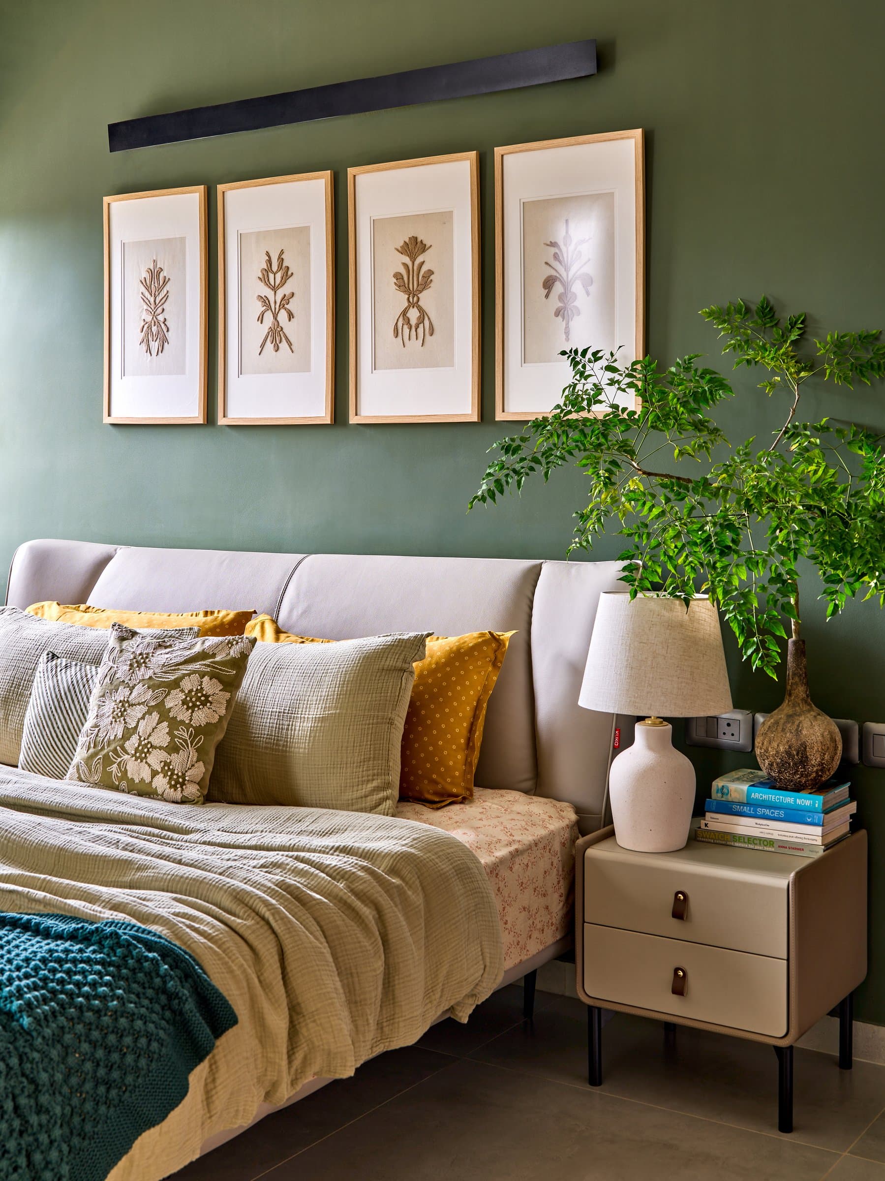 The headboard wall at closer range, where framed botanicals and an upholstered side table soften the green envelope