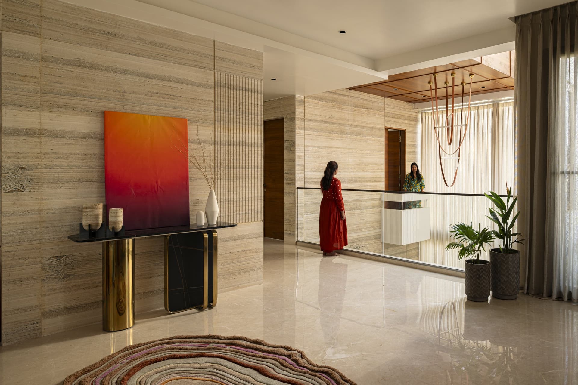 The upper lobby, where a travertine wall and a brass-and-stone console establish the home's material grammar before any room is entered