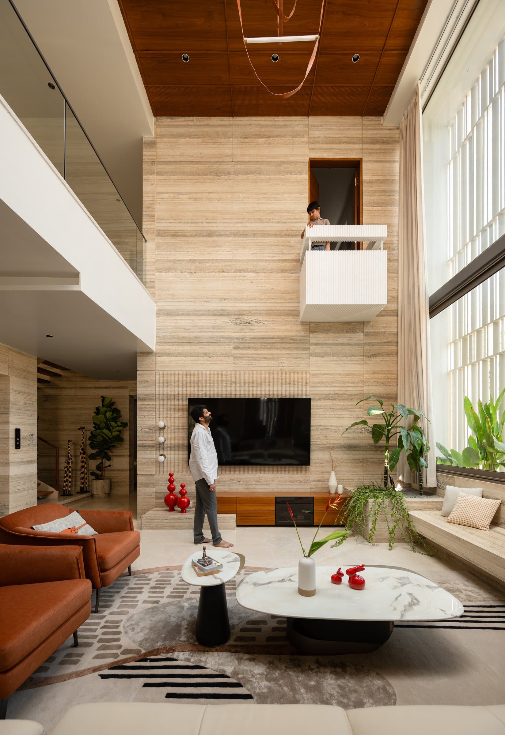 The double-height living room, with its cantilevered upper balcony projecting from a continuous travertine wall