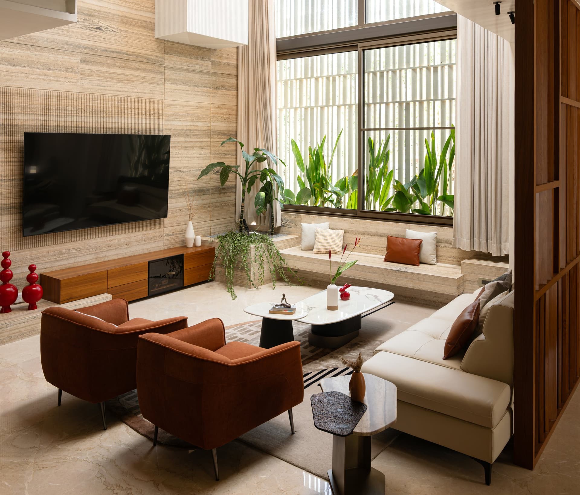At the lower seating zone, rust-toned armchairs gather around a sculptural marble-topped table against a ribbed travertine wall