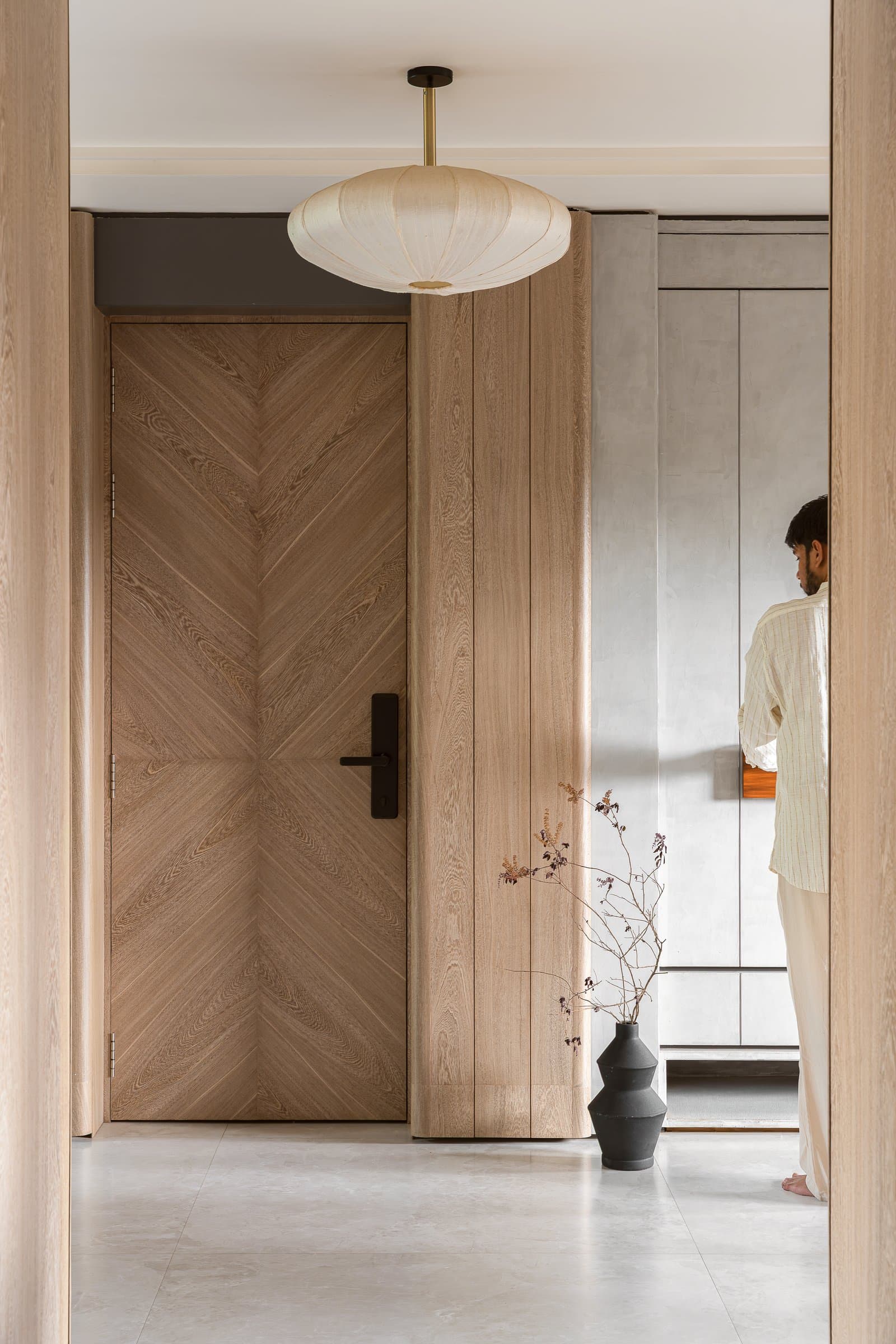 The threshold: a chevron-grain door and a single linen pendant set the home's tonal grammar before a visitor steps inside
