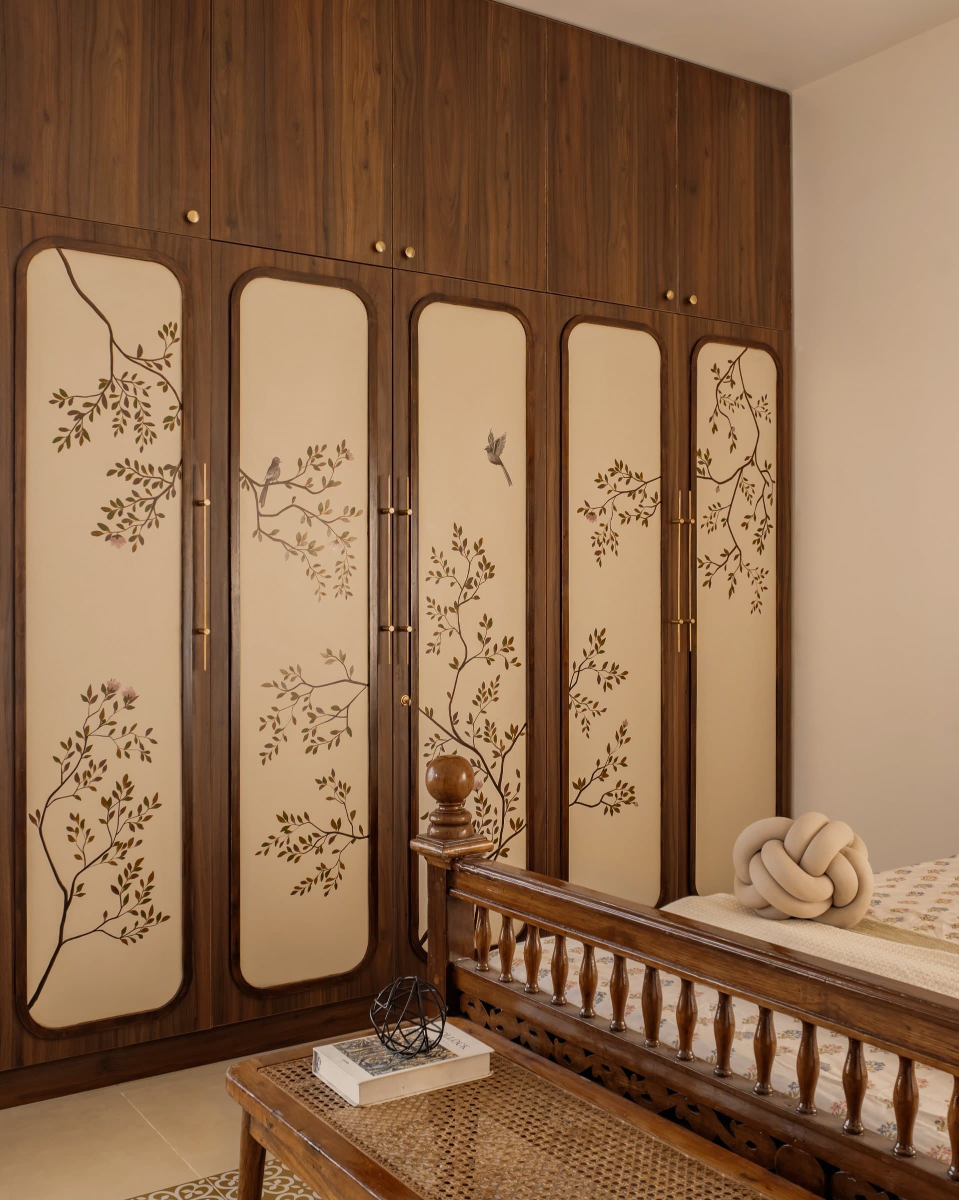 The wardrobe, with five arched cream panels hand-painted with branching foliage and birds, framed in warm wood