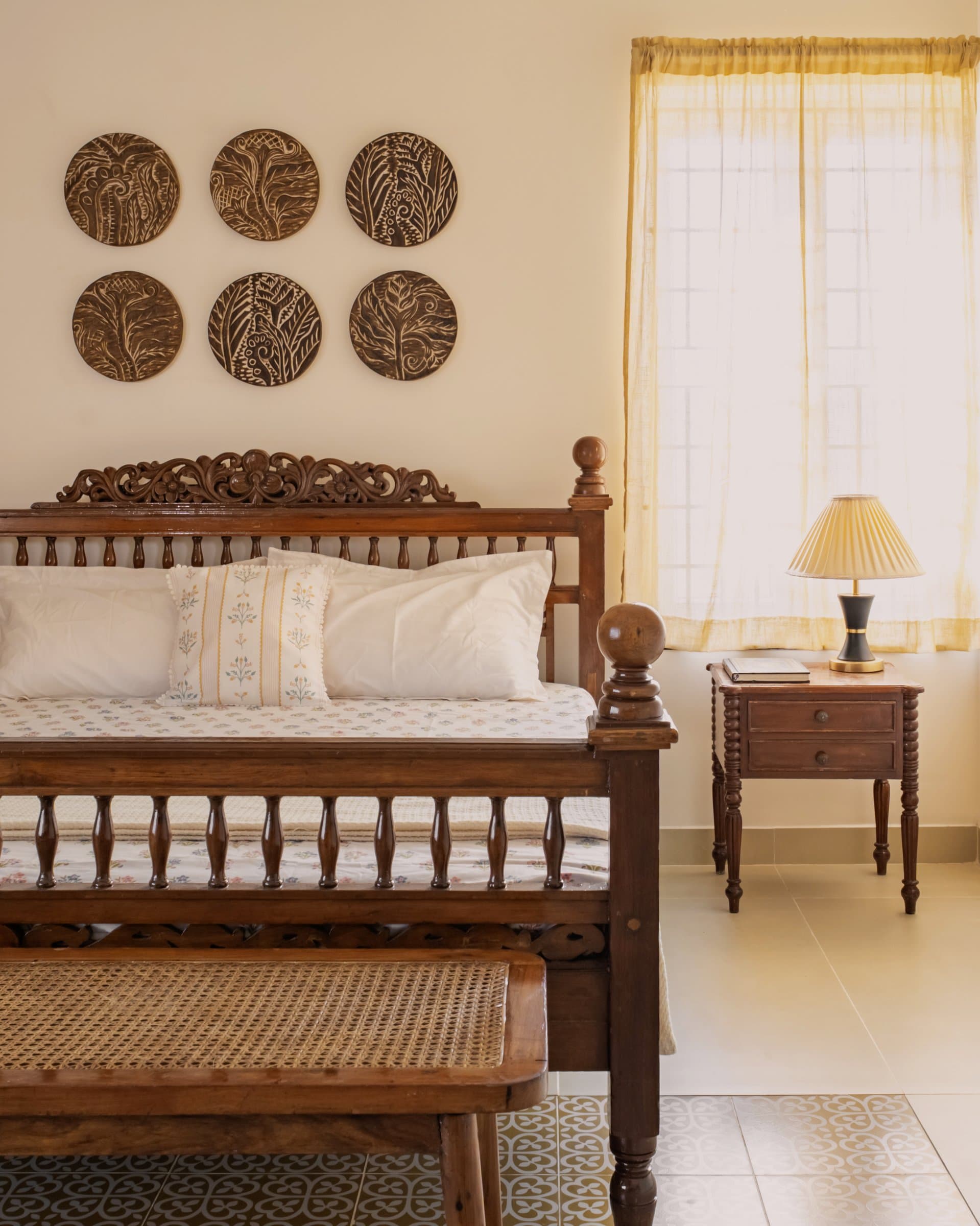 A closer view of the spindled bed, its carved crest, and a turned-leg bedside table with a pleated shade