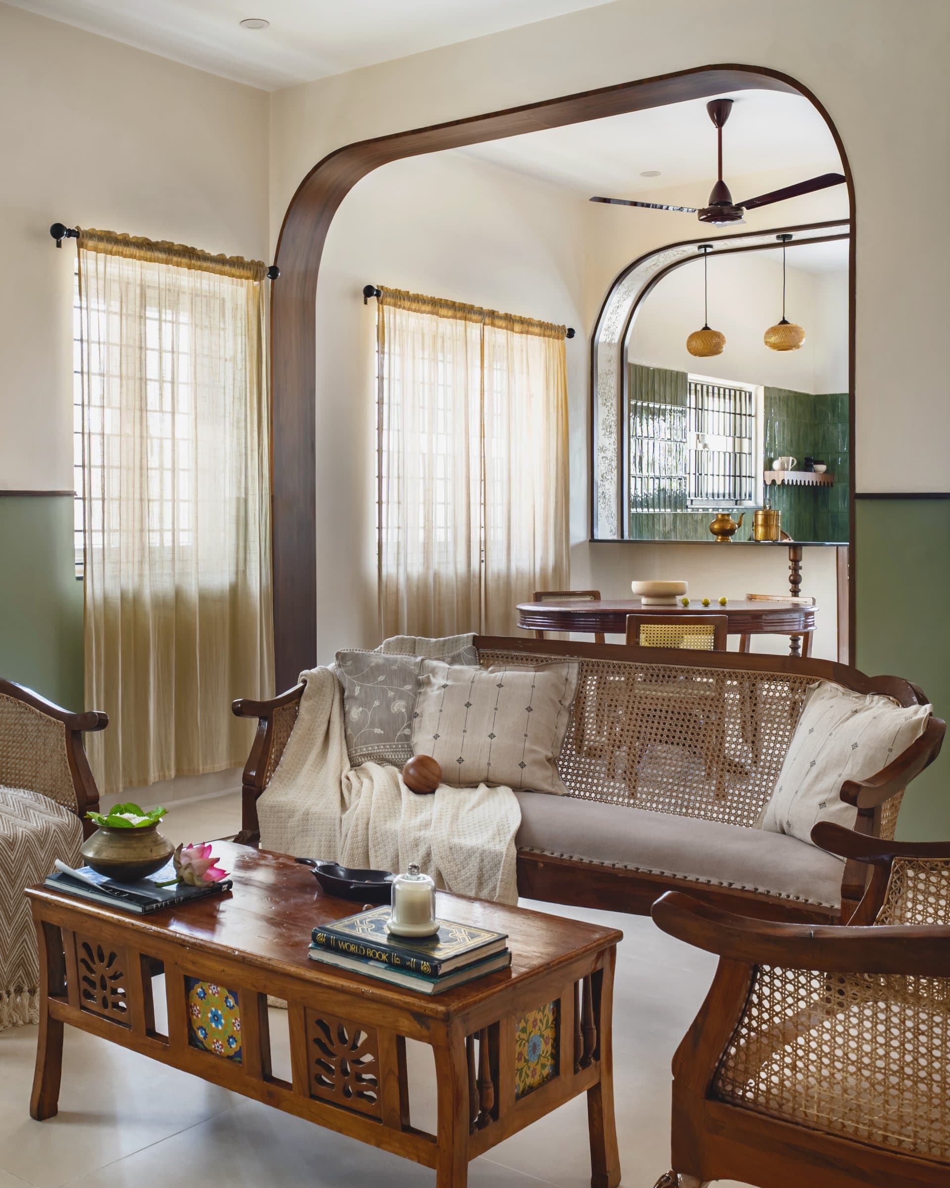The living room, paced by sheer light and a caned teak settee set behind a low coffee table with inset painted tiles