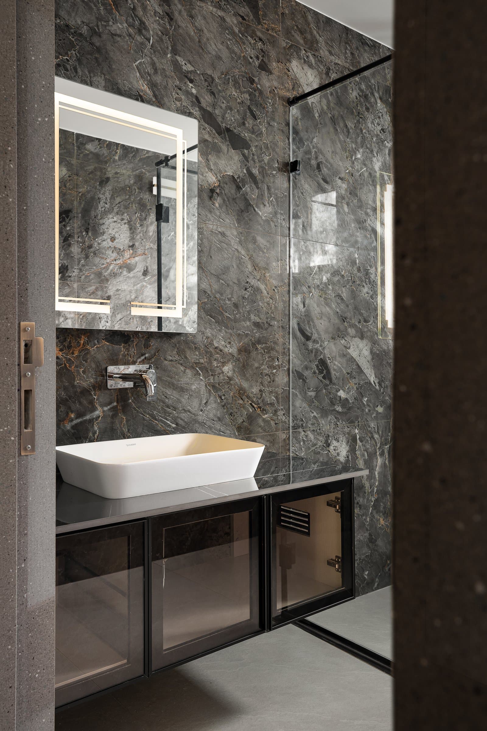 The second bathroom moves darker: dramatically veined stone meets a black-framed glass vanity