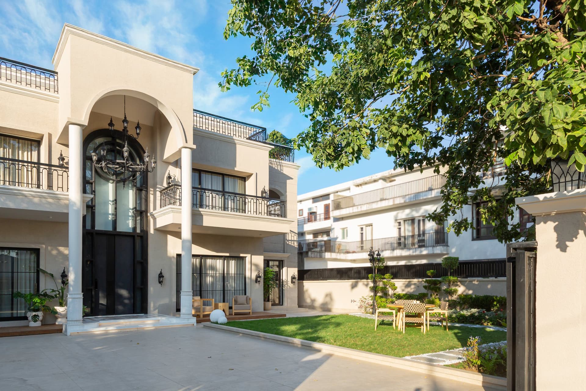 The villa's exterior: a tall central arch frames the entrance, flanked by slim fluted columns and the mature tree that shaped the home's view corridors