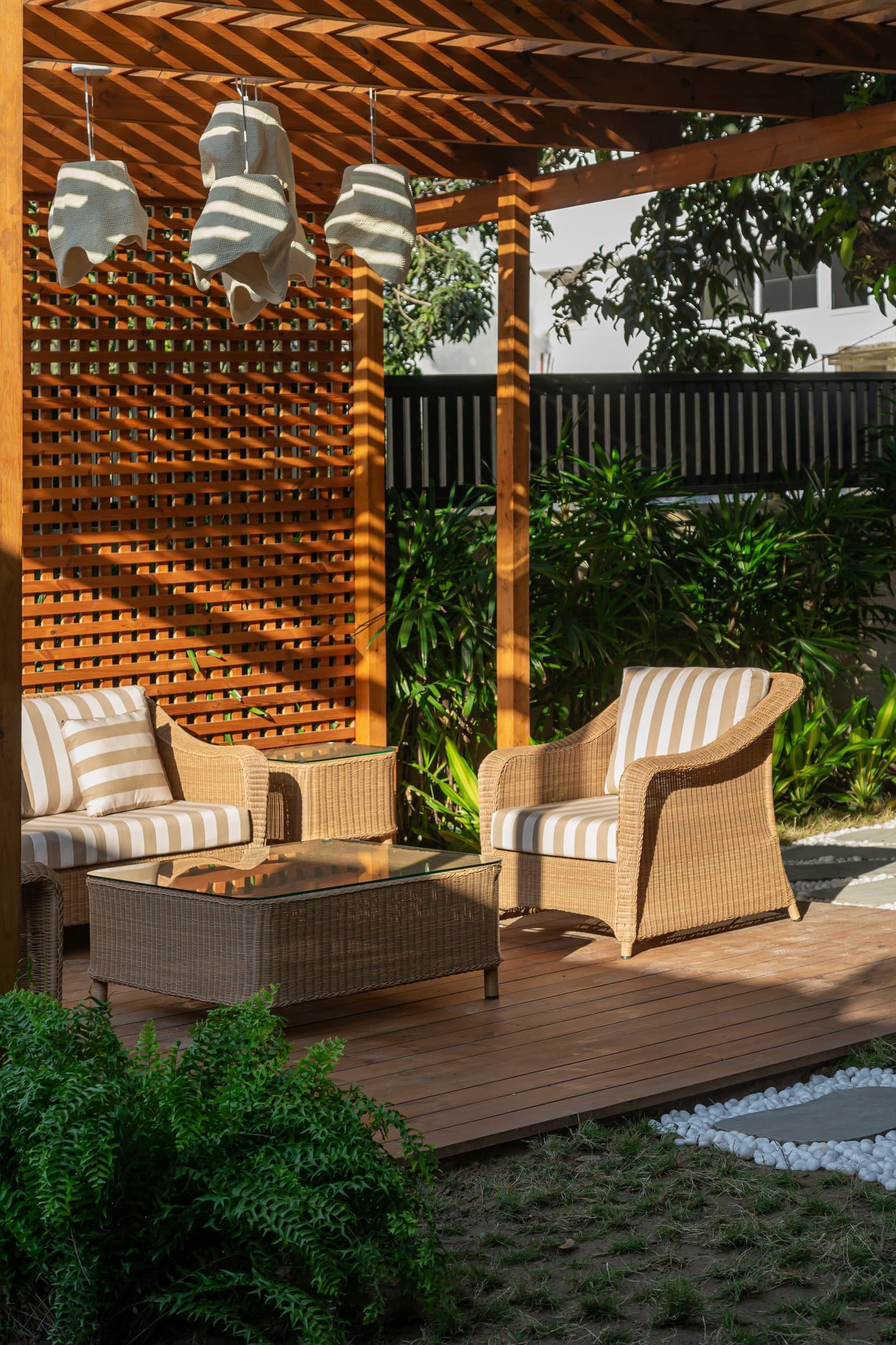 The garden deck: a wooden pergola filters sunlight onto rattan armchairs and fabric pendants