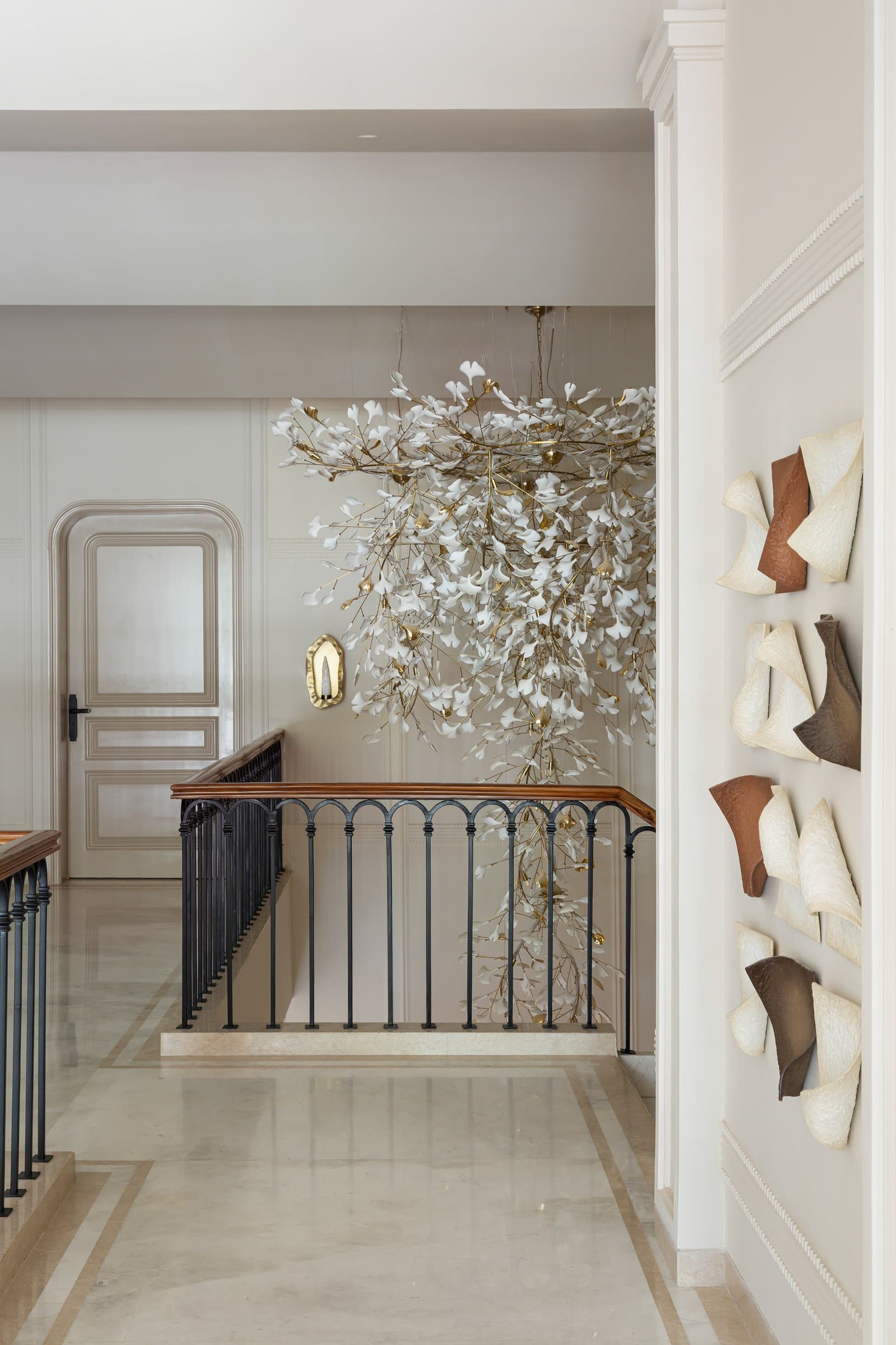 The first-floor landing, where a second porcelain-and-brass chandelier cascades into the double-height void