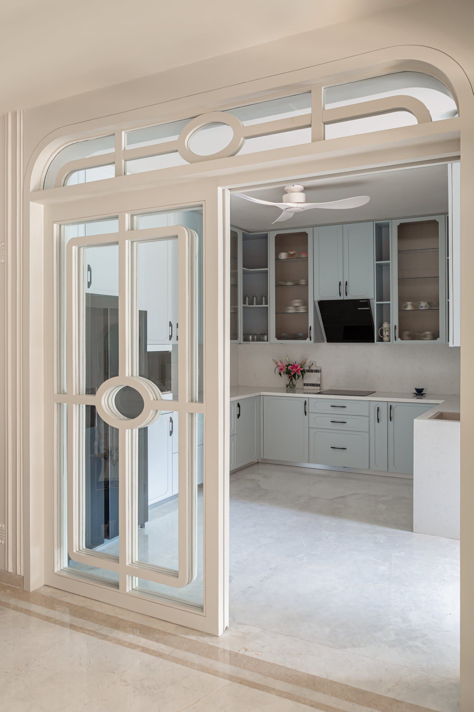 The threshold to the kitchen: a sliding glass-and-cream door with Georgian bars and a porthole motif within a softly arched frame