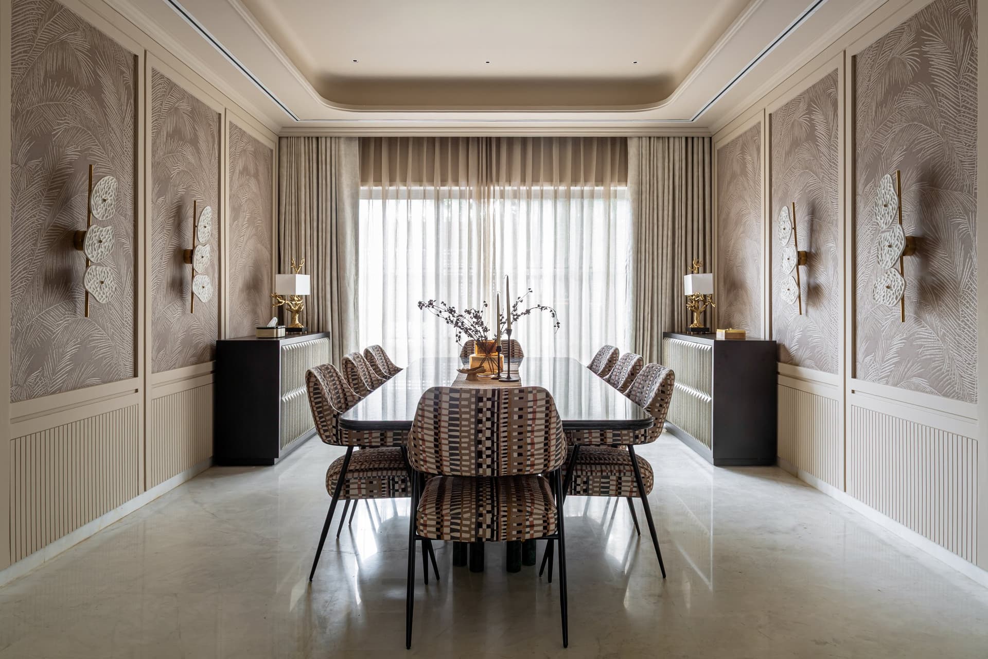 The dining room, where palm-frond wall paper rises above fluted wainscoting and a long dark-stone table anchors the room between twin consoles