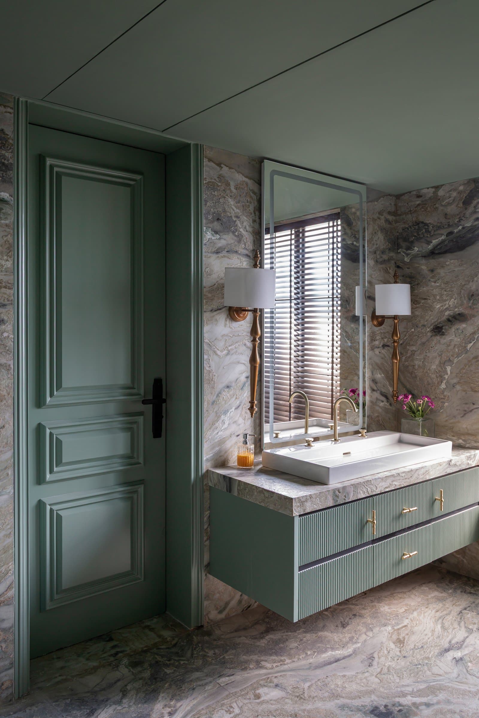 The bathroom permits itself colour: a sage-green panelled door and fluted cabinet against dramatically veined stone
