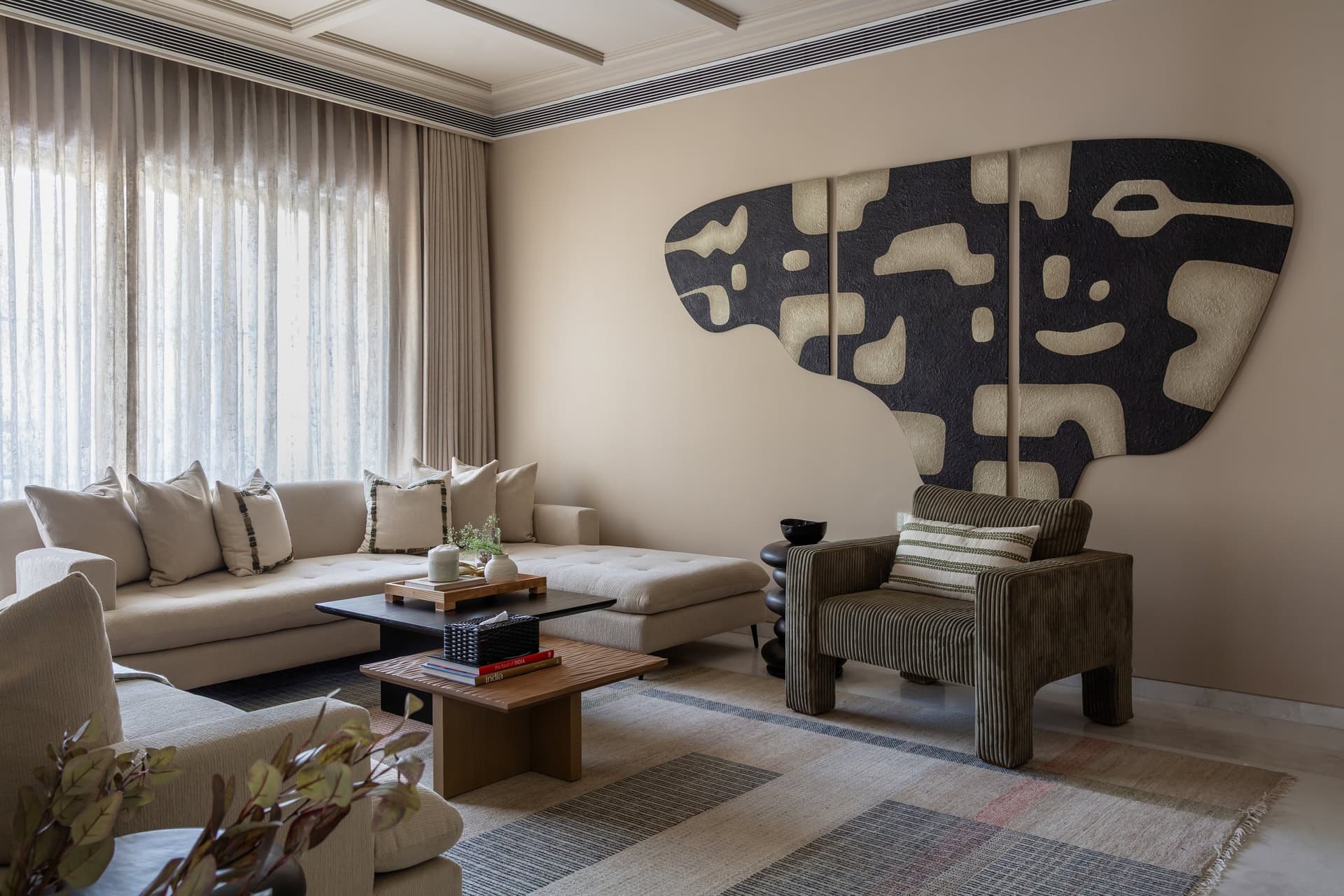 The family lounge, where an unbleached cream sectional and ribbed olive armchair are anchored by a large biomorphic triptych in matte black and bone
