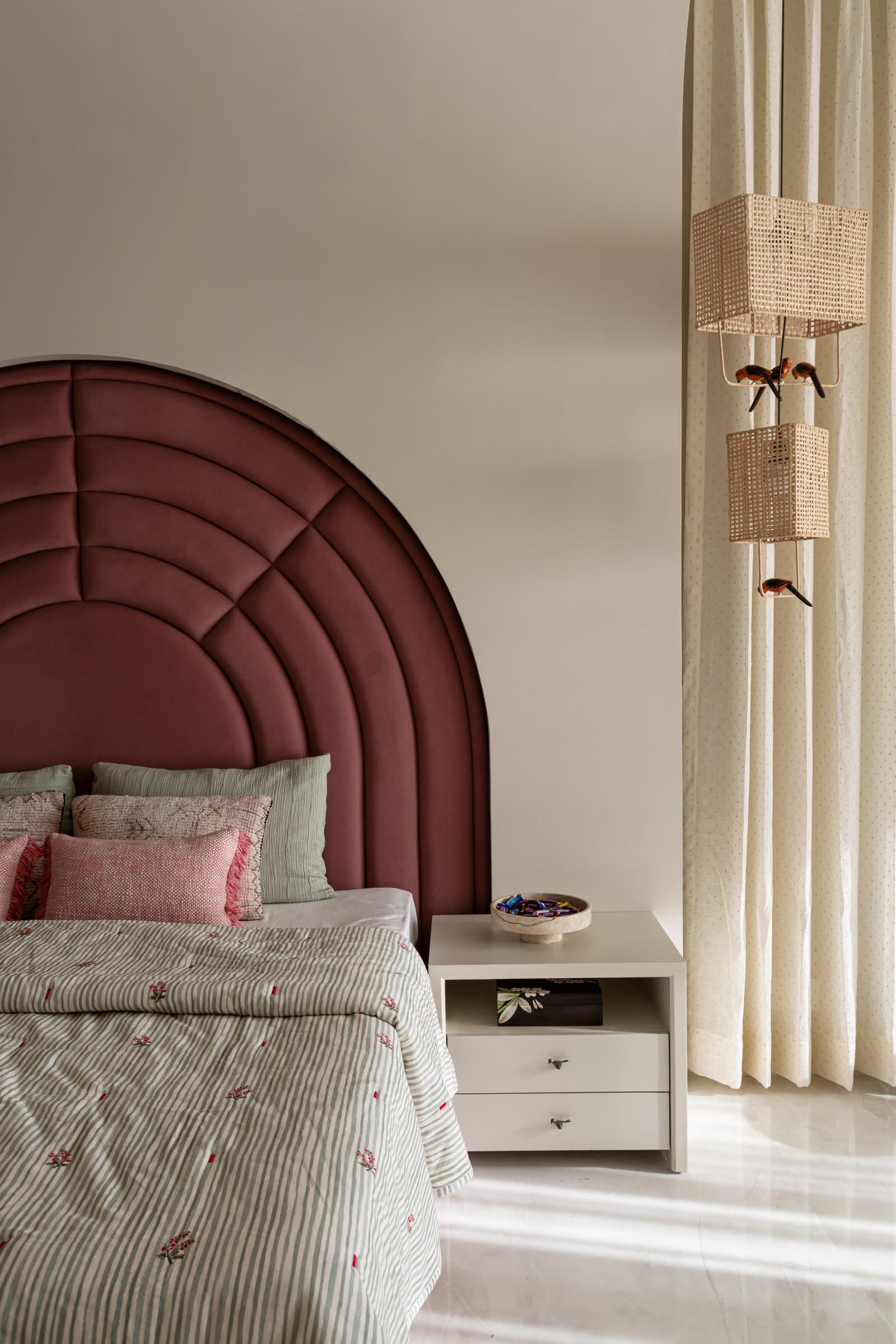 The daughter's room: an arched headboard in dusty rose, channel-tufted in concentric rings, with rattan lanterns hanging alongside